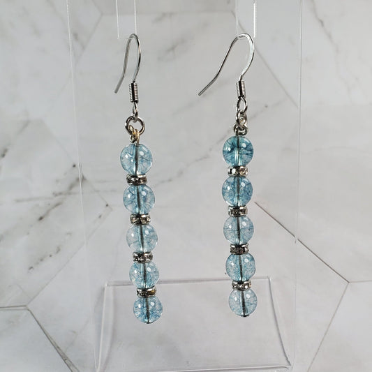 Pair of beaded earrings on a clear stand against a marble background