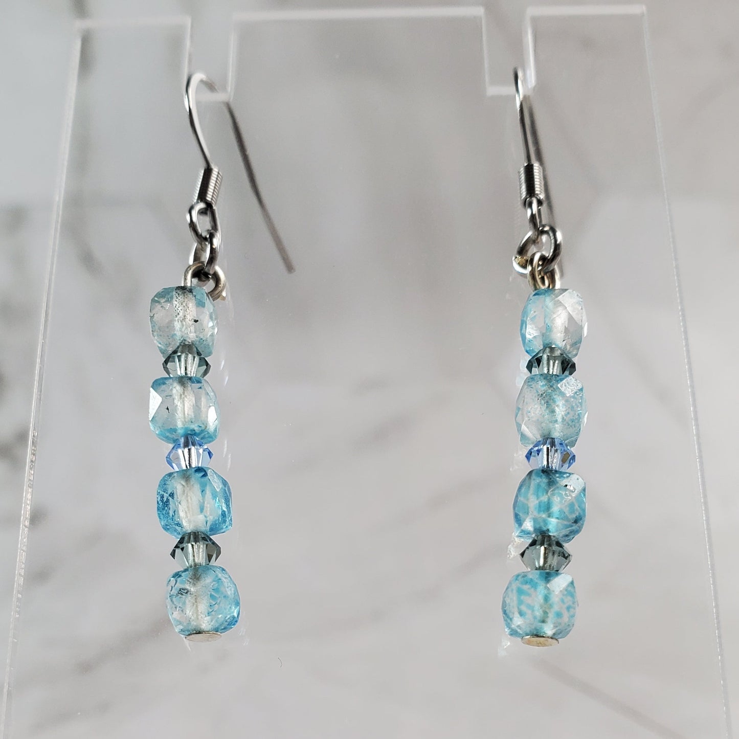 Pair of beaded earrings on a clear stand against a marble background