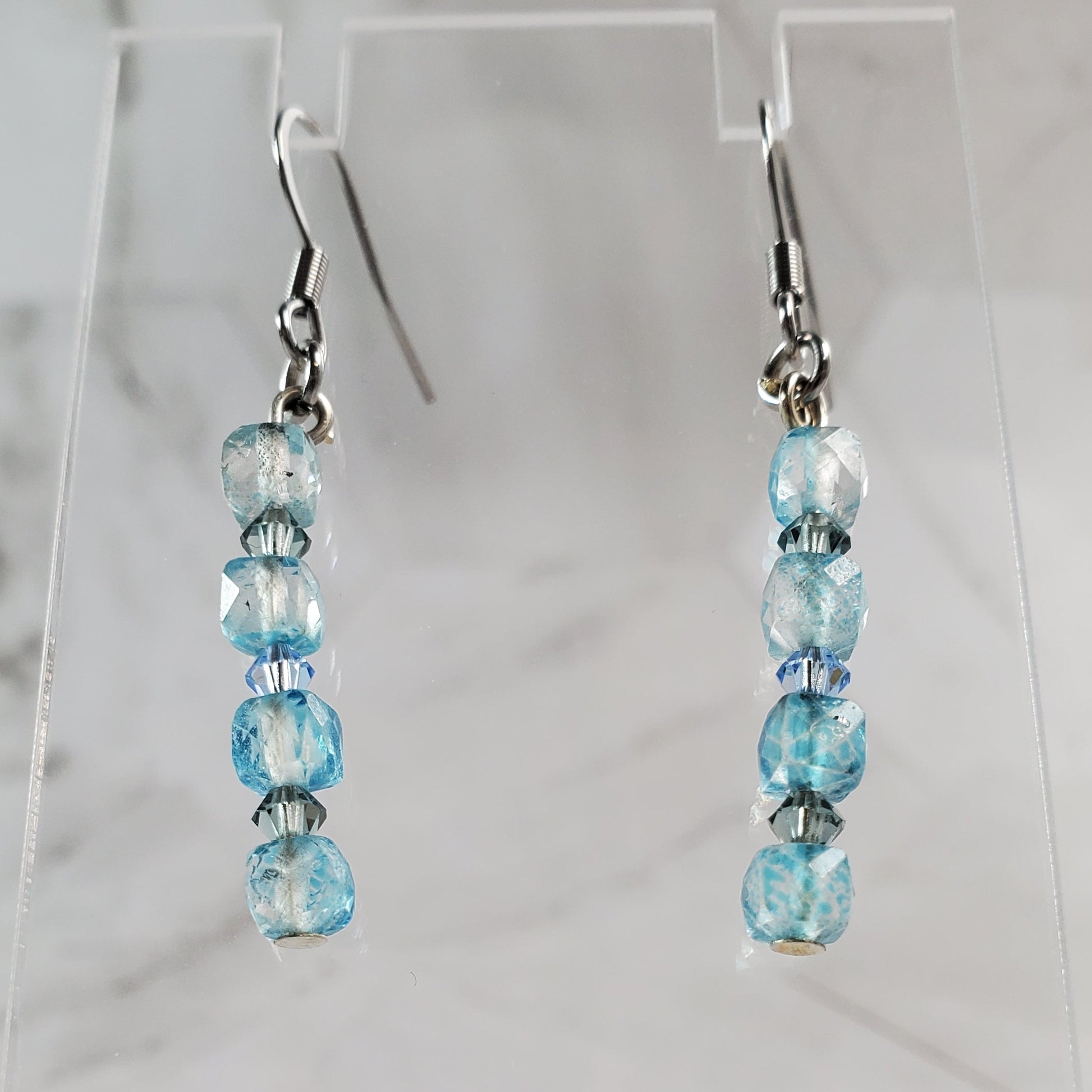 Pair of beaded earrings on a clear stand against a marble background