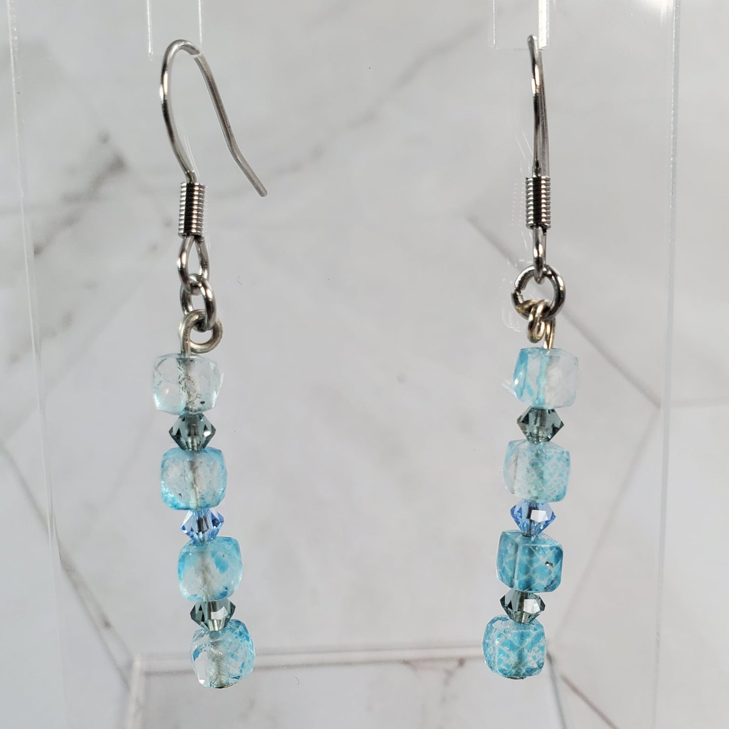 Beaded earrings on a clear stand against a marble background