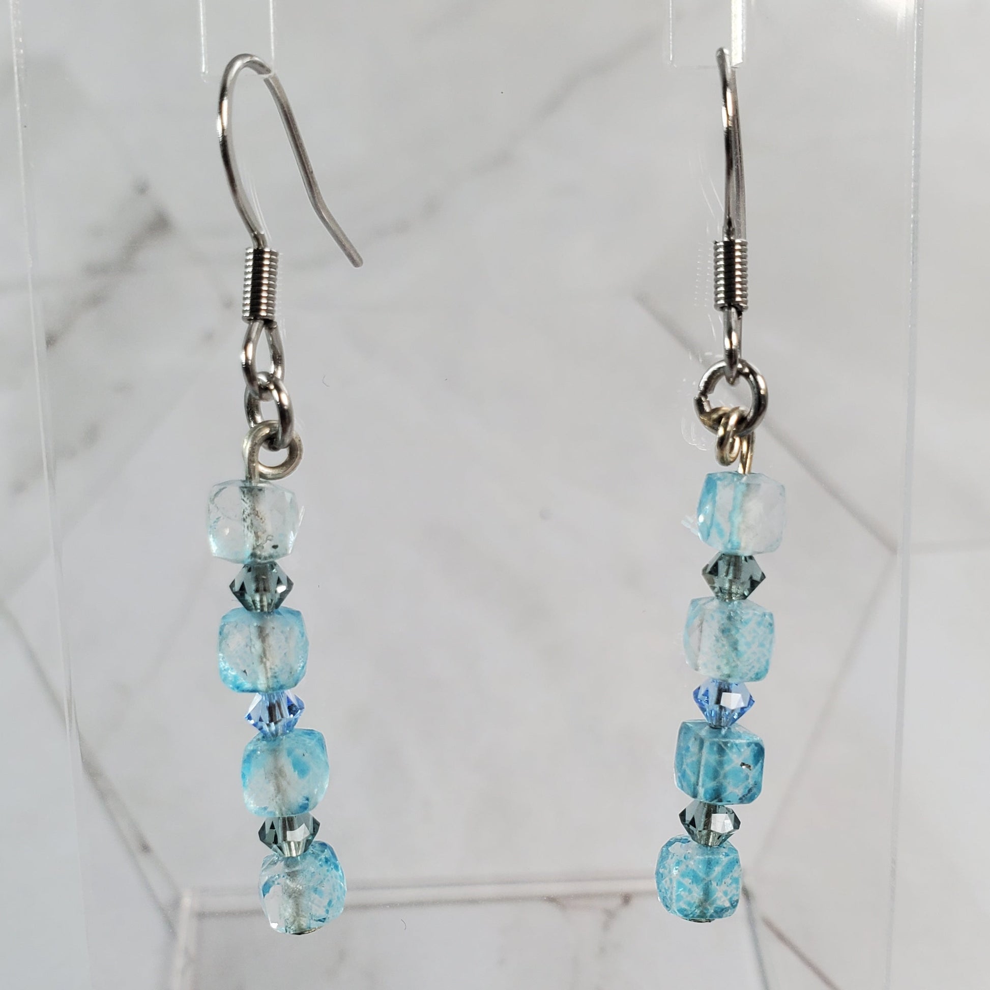 Beaded earrings on a clear stand against a marble background