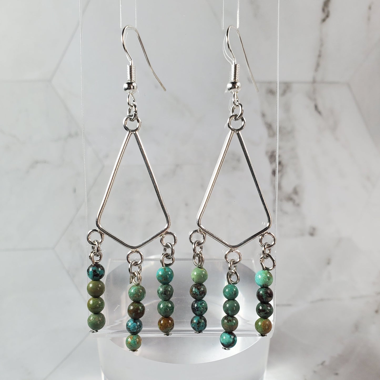Beaded earrings on a white stand against a marble background