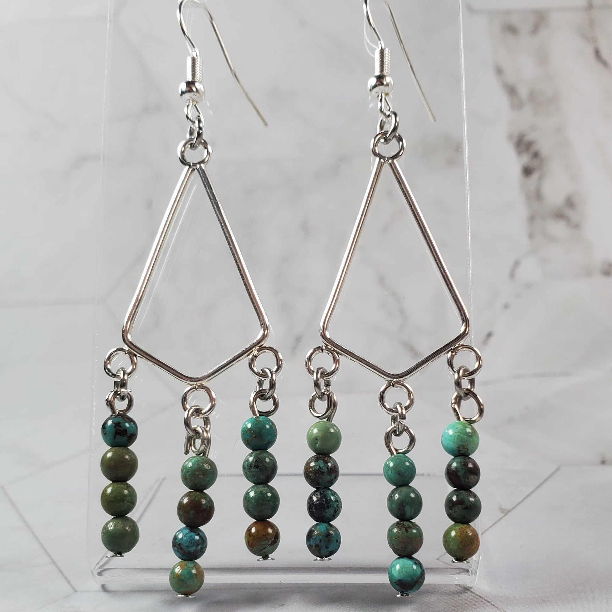 Pair of earrings with green beads hanging from silver teardrop pendants on a marble surface.