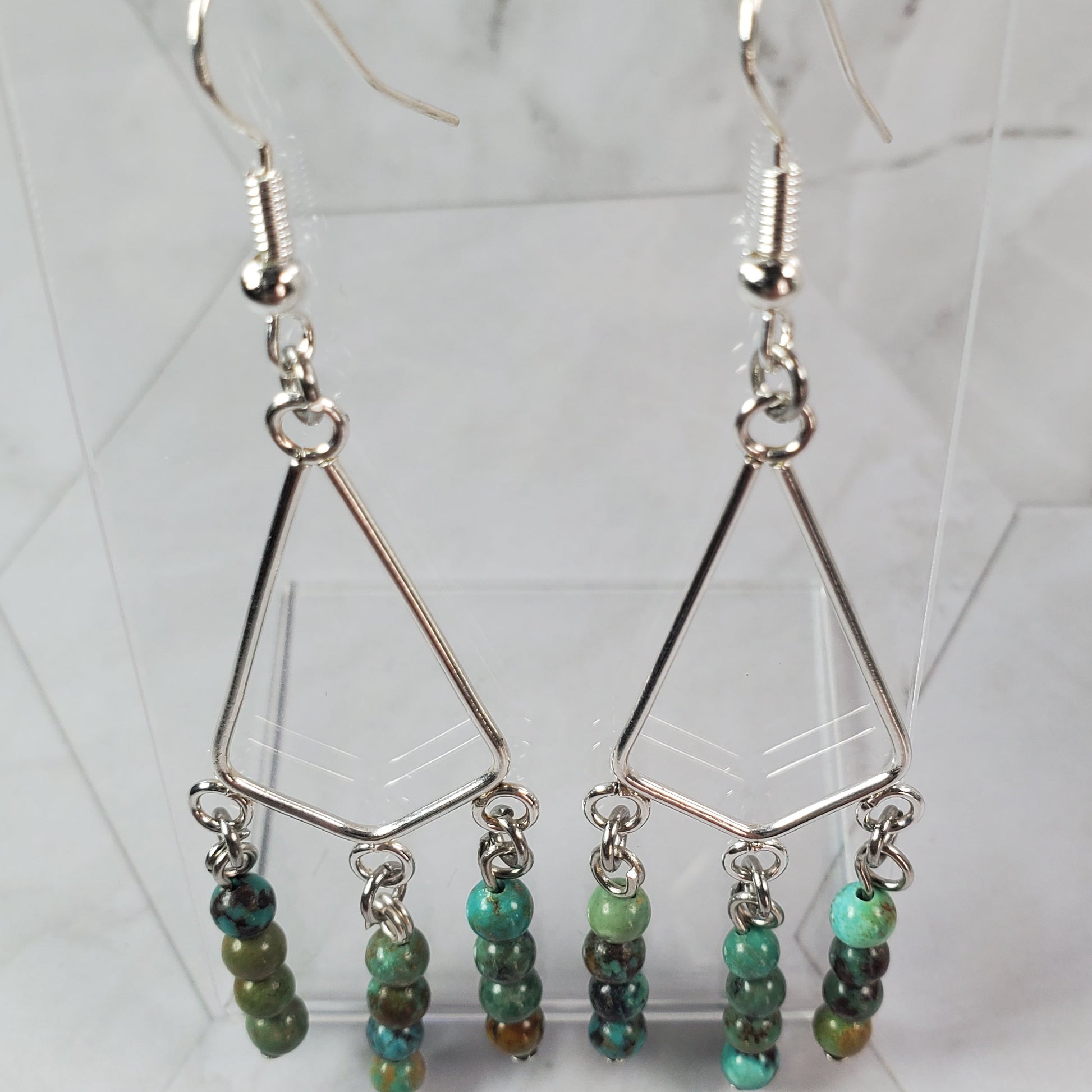 Pair of earrings with green beads on a marble surface