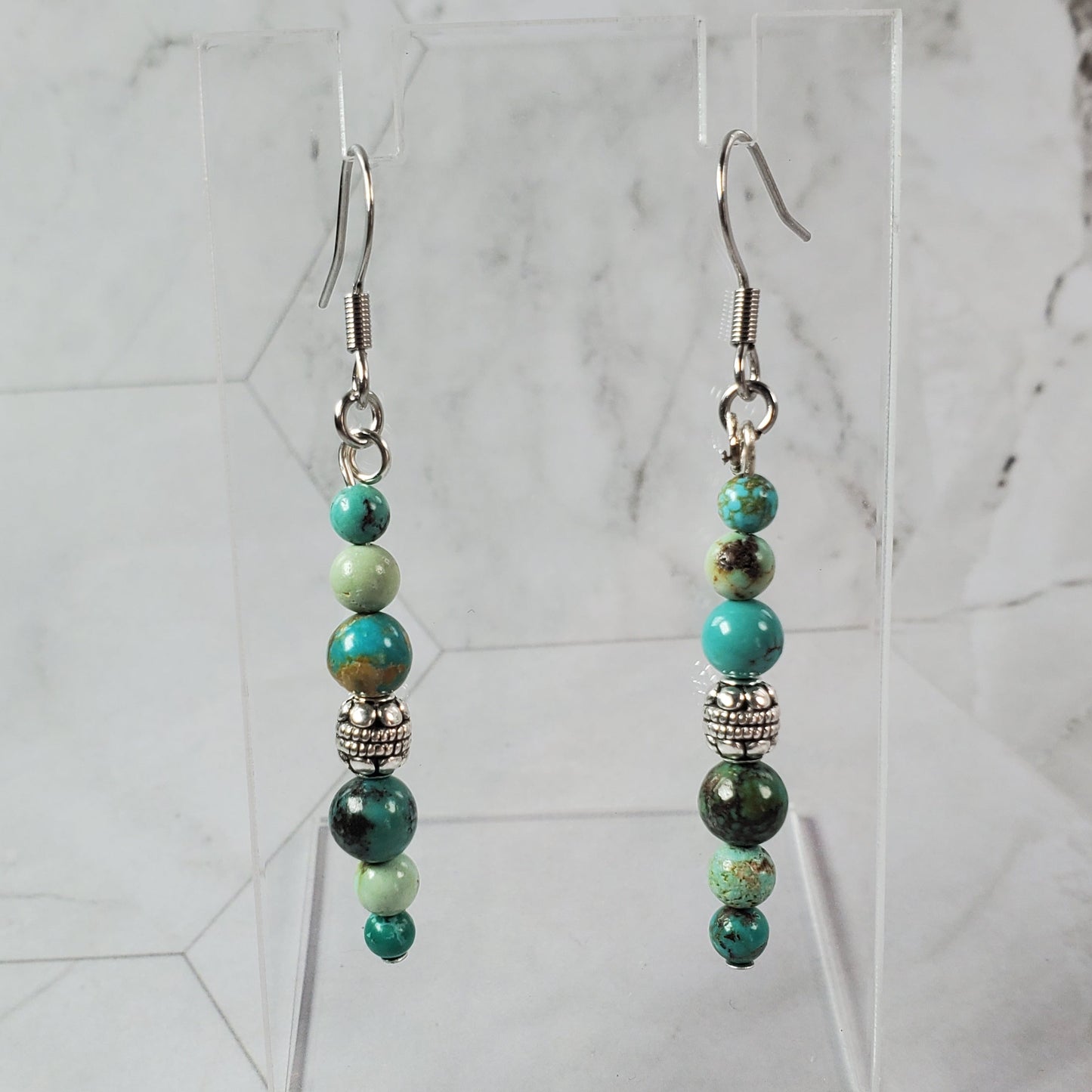 Pair of green beaded earrings on a clear stand against a marble background