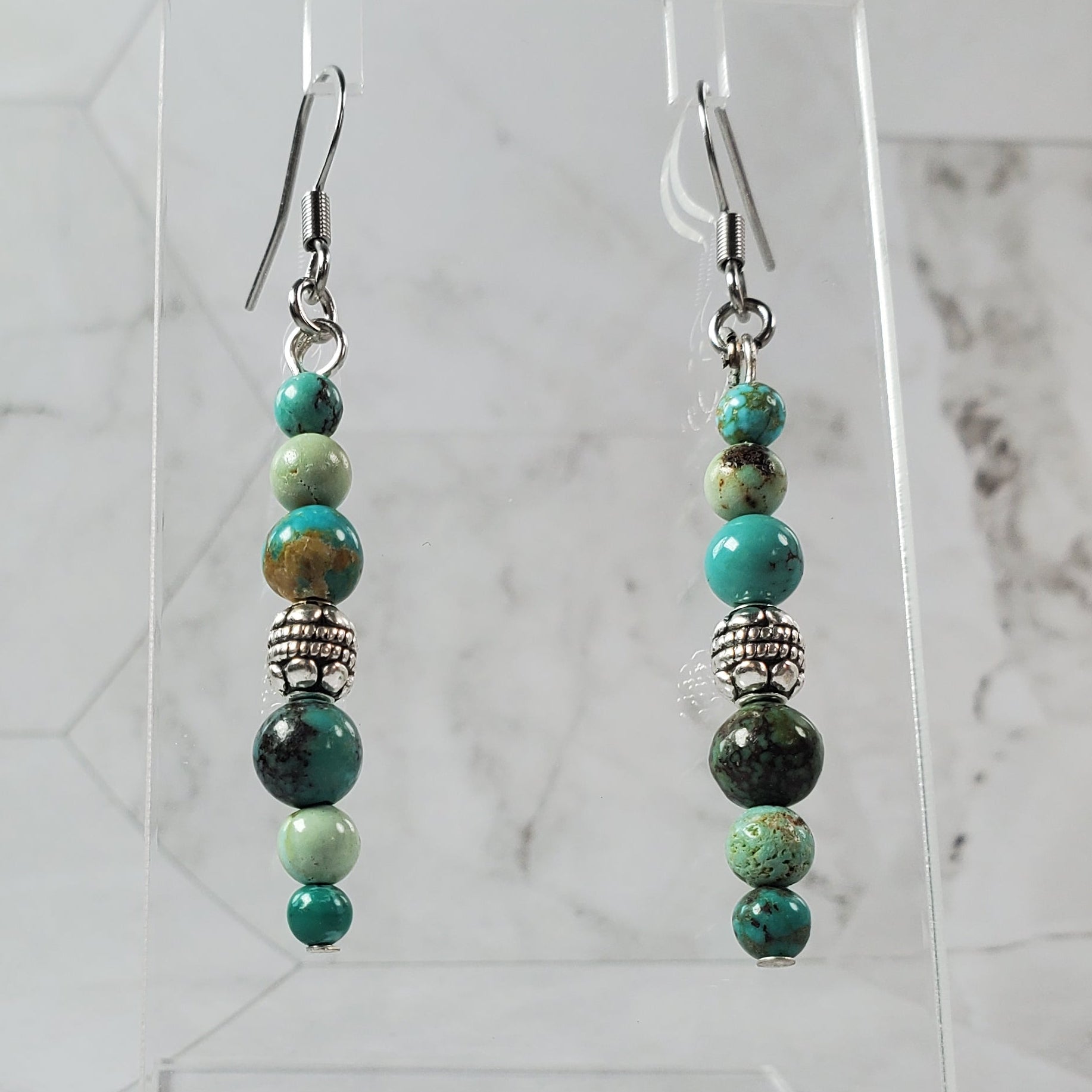 Pair of beaded earrings on a clear stand against a marble background