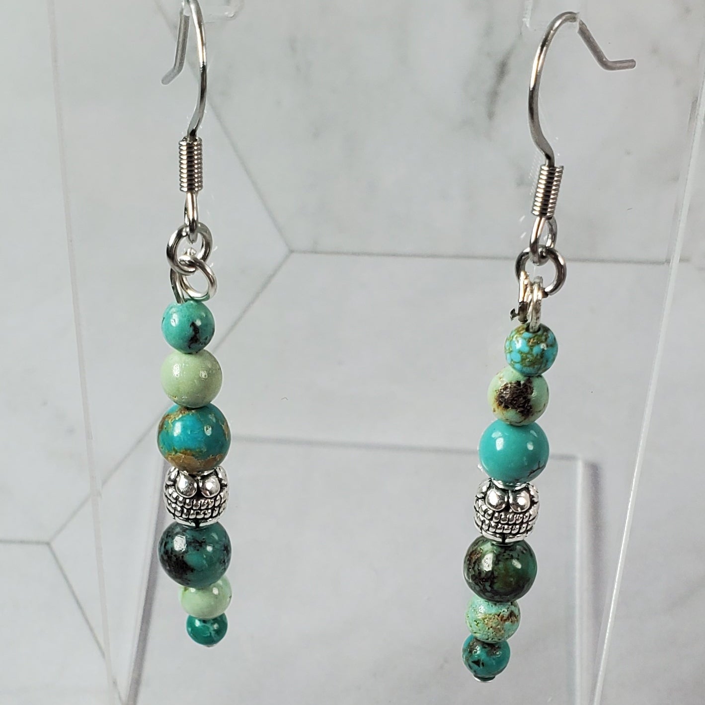 Beaded earrings on a marble surface with a mirror reflection.