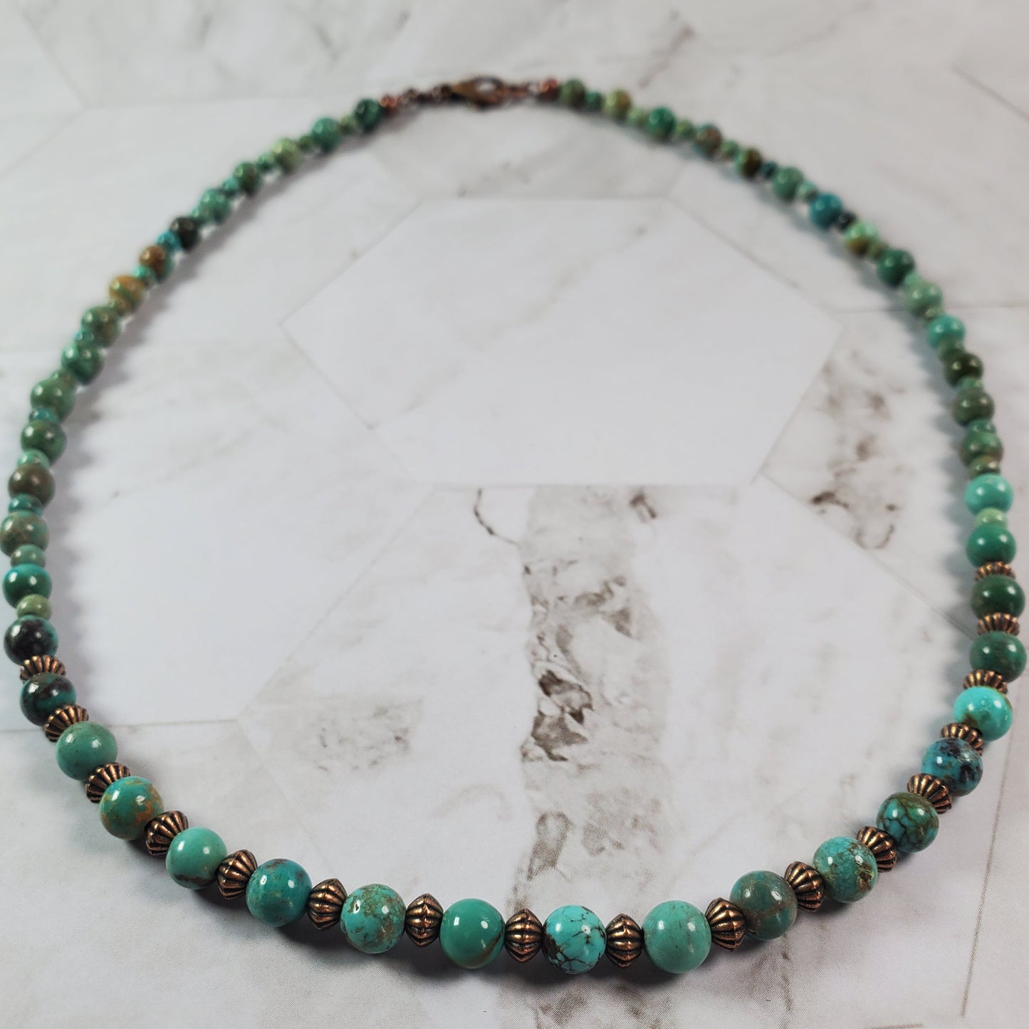 Beaded necklace with green and brown beads on a marble surface