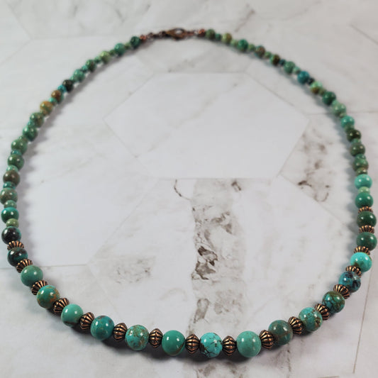 Beaded necklace with green and brown beads on a marble surface