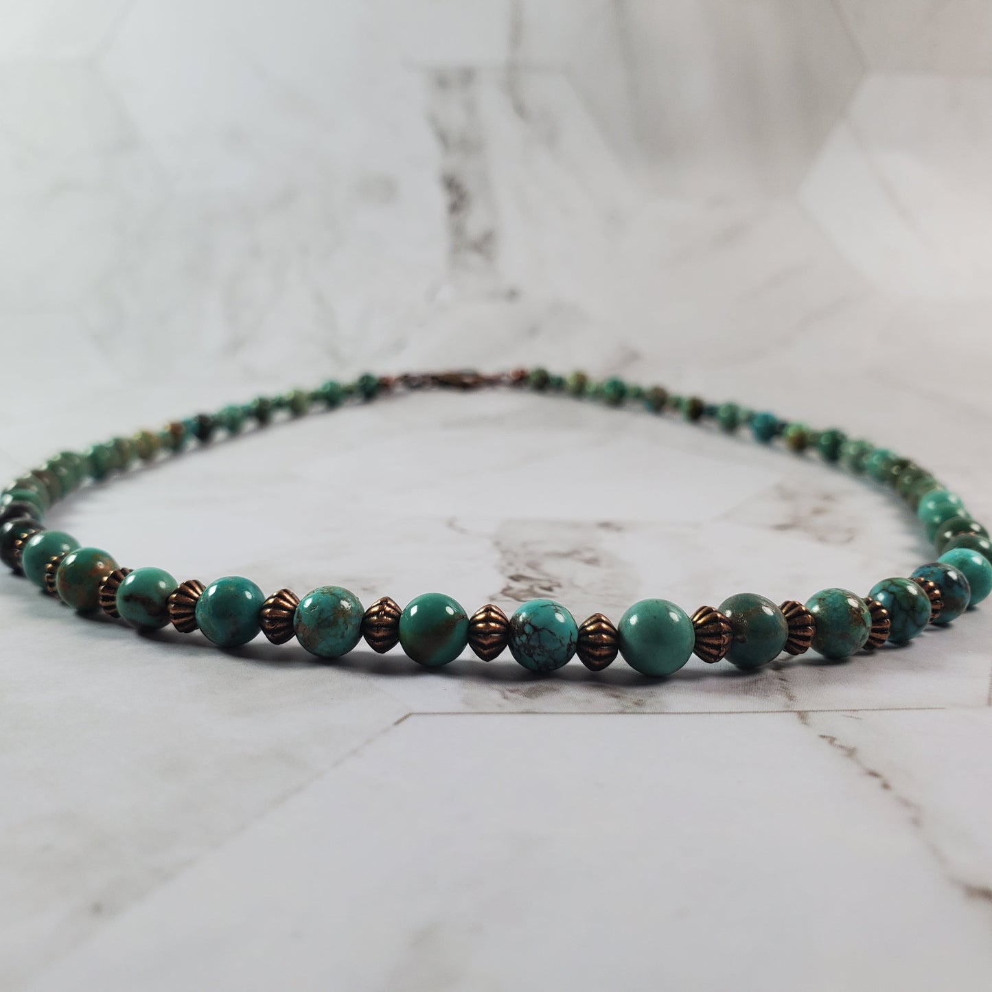 Beaded necklace with green and brown beads on a marble surface