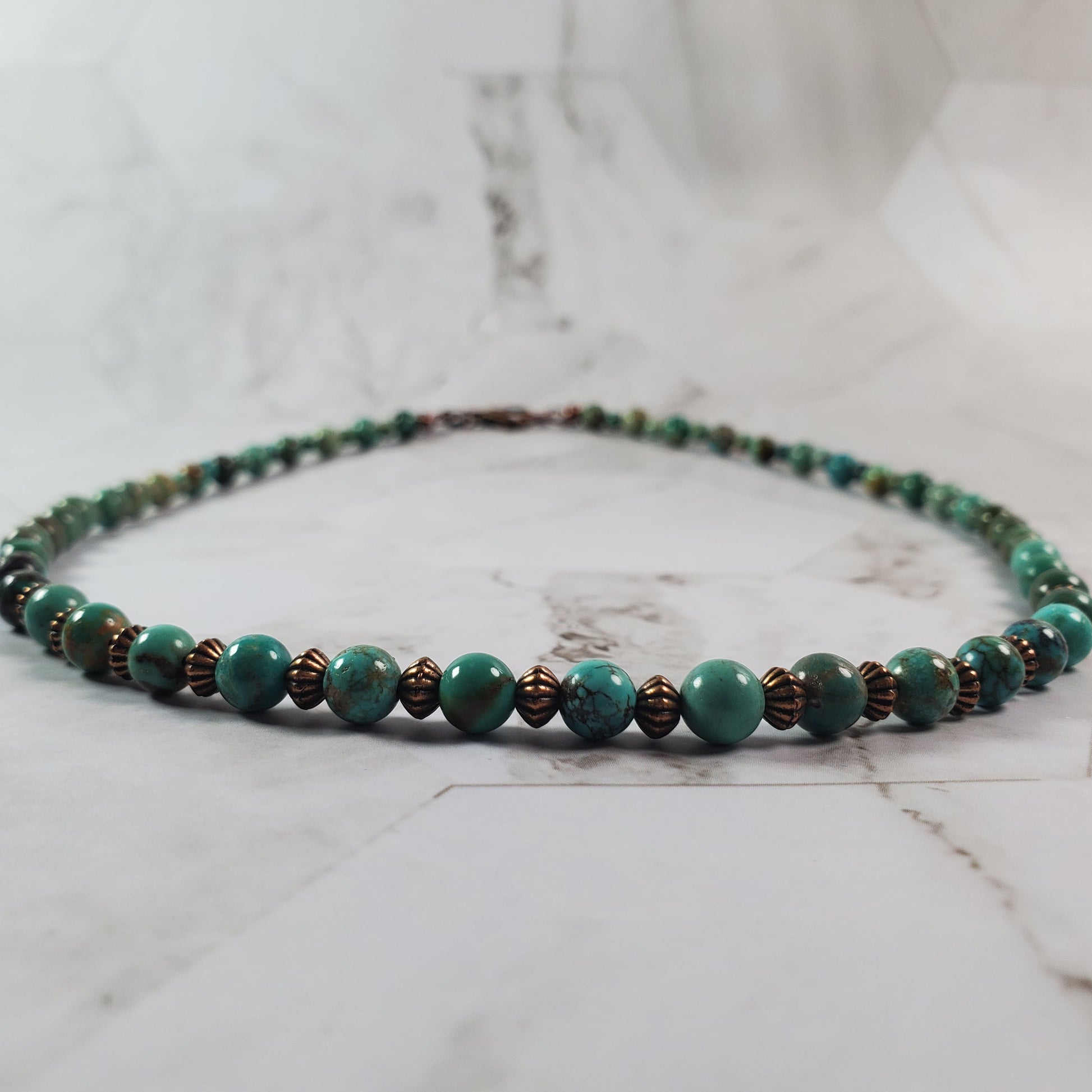 Beaded necklace with green and brown beads on a marble surface
