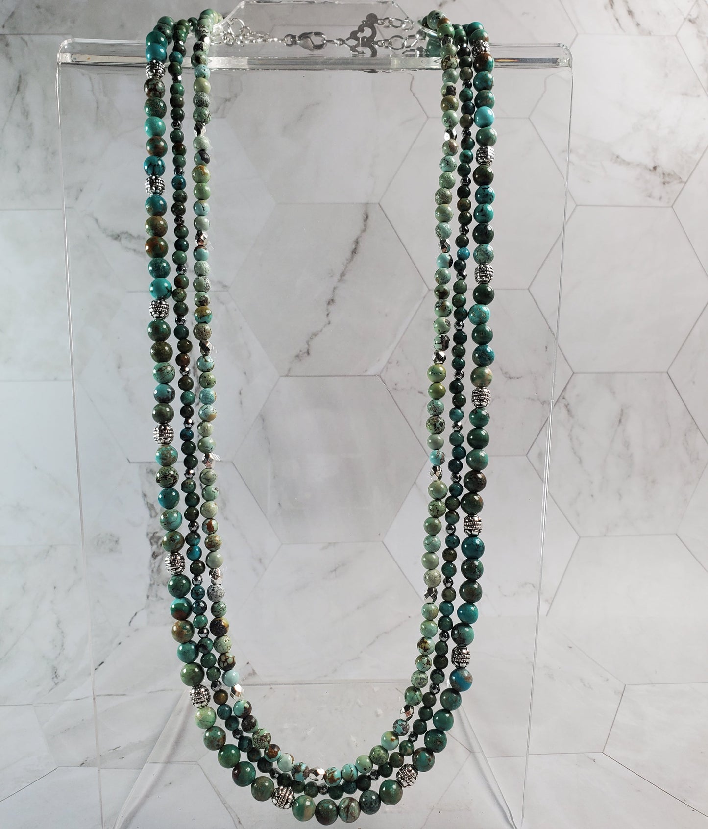 Multistrand beaded necklace on a clear stand against a marble background