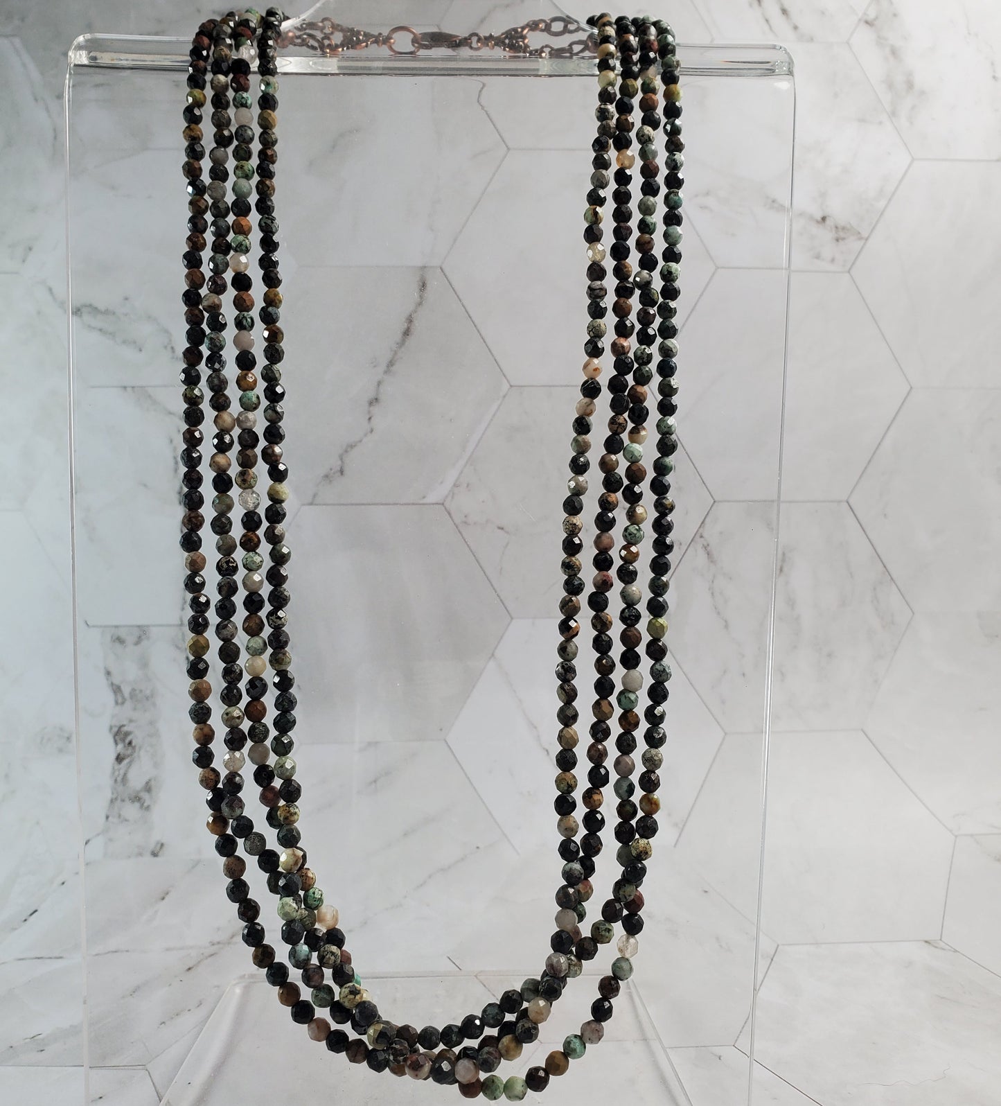 Beaded necklace on a clear stand against a marble background