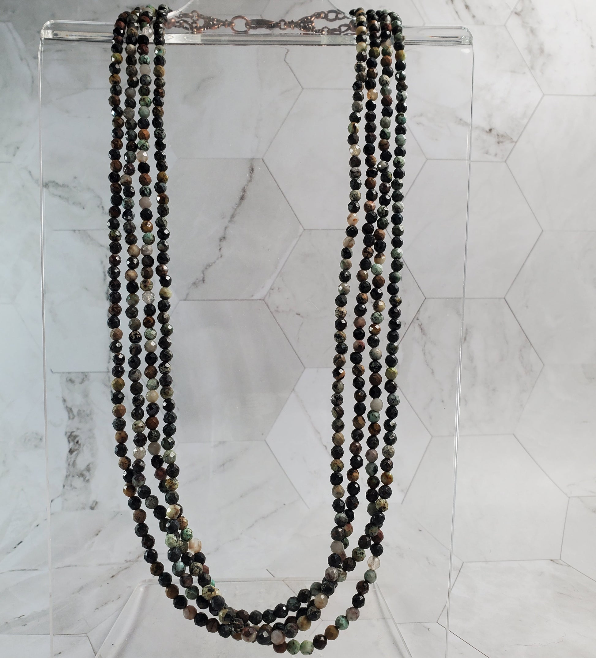 Beaded necklace on a clear stand against a marble background