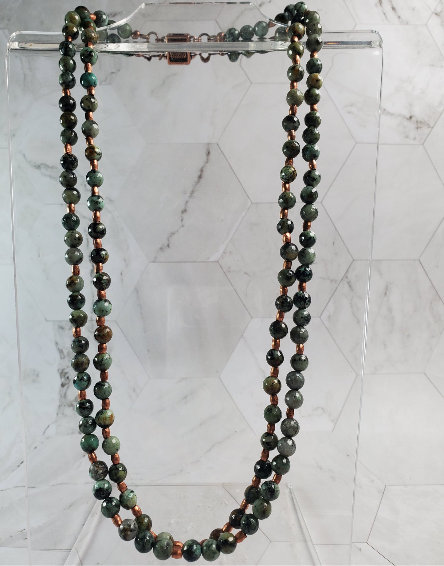 Green beaded necklace on a clear stand against a marble background