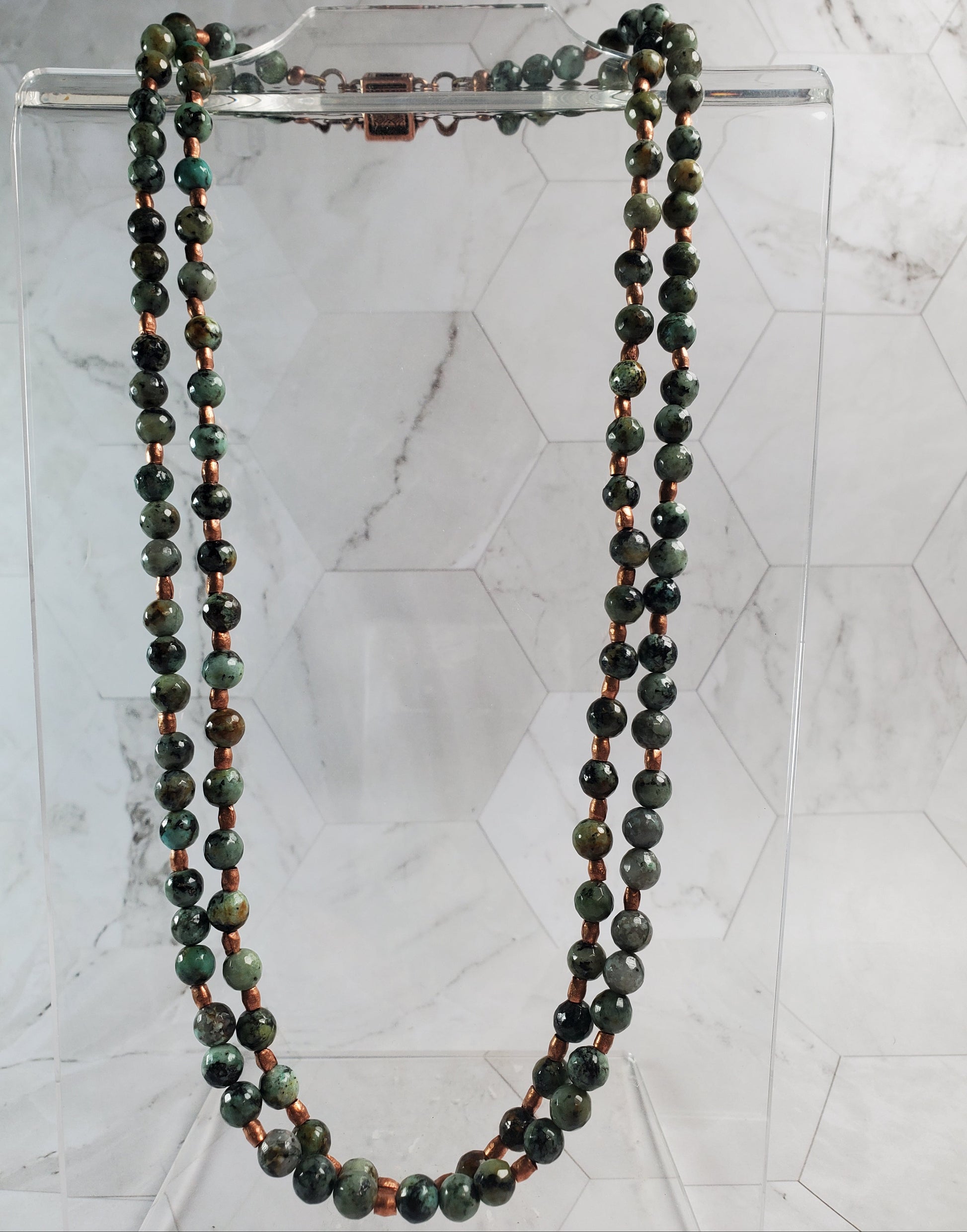 Green beaded necklace on a clear stand against a marble background