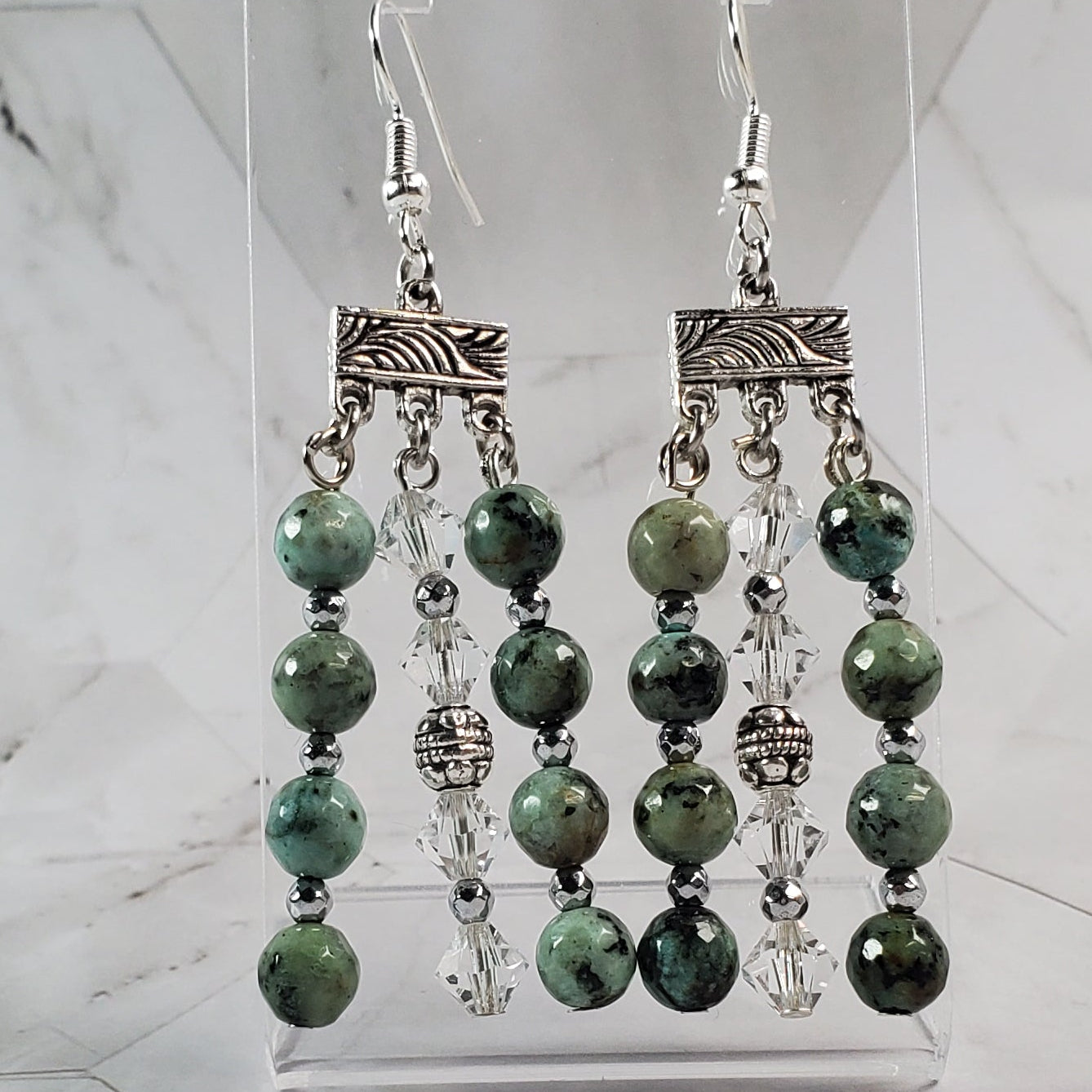 Green beaded earrings on a clear stand against a marble background
