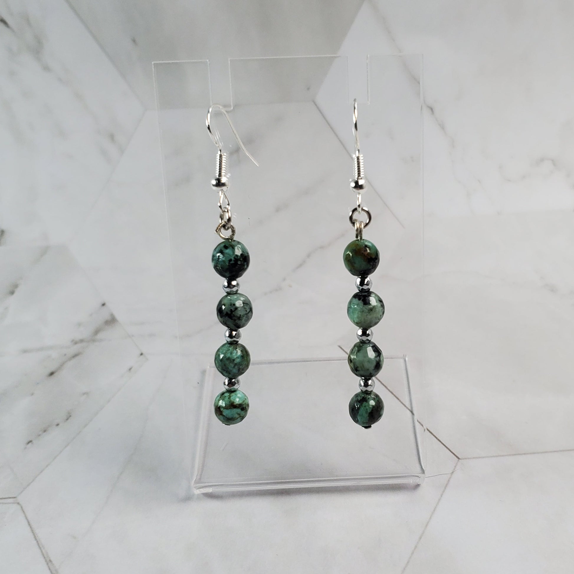 Pair of earrings with green beads on a marble surface