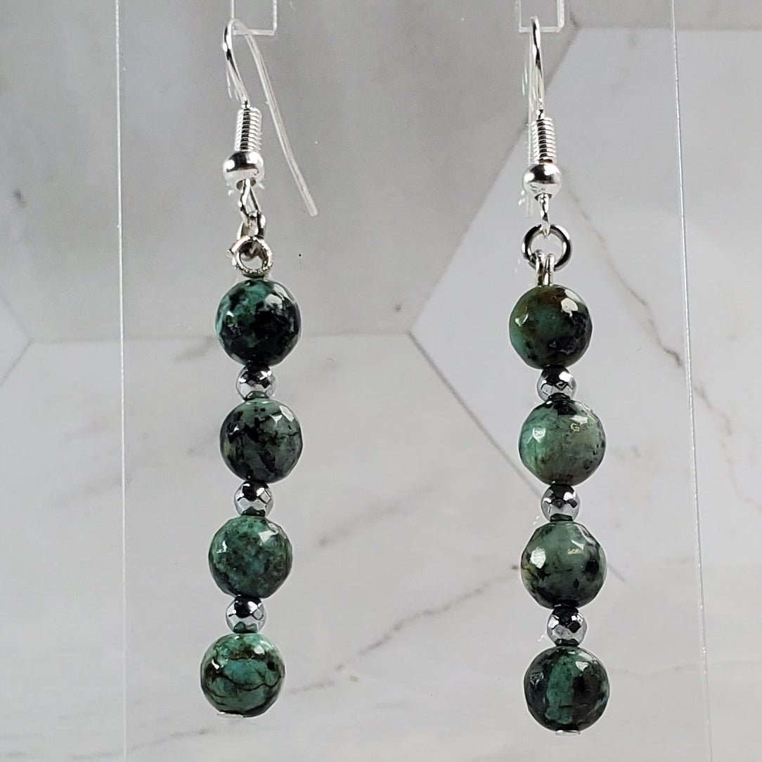 Green beaded earrings on a clear stand against a marble background