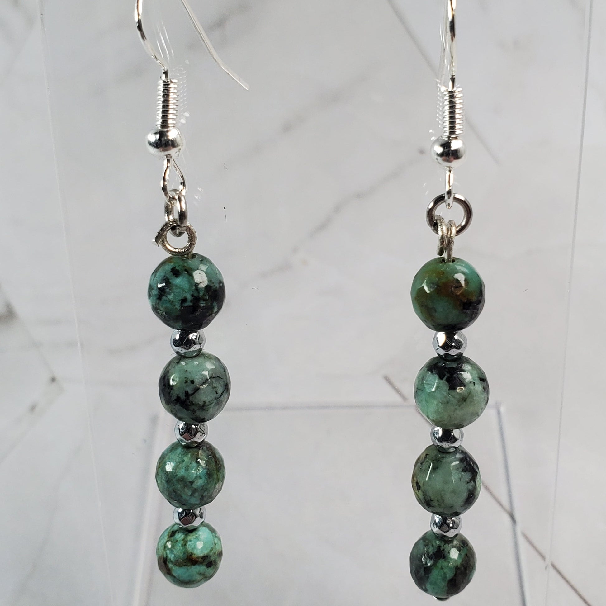 Green beaded earrings on a clear stand against a marble background