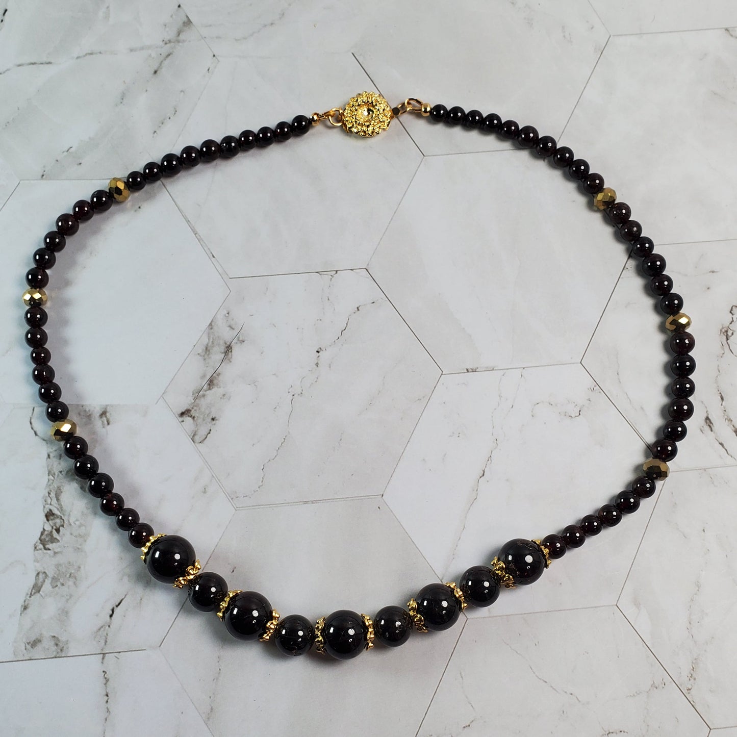 Necklace with deep red beads and gold accents on a marble surface