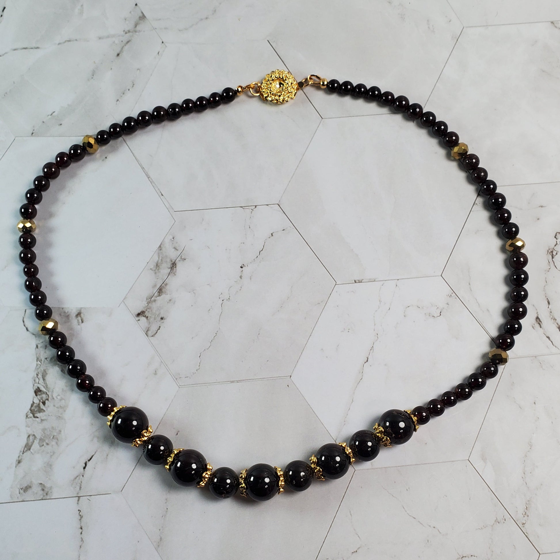 Necklace with deep red beads and gold accents on a marble surface