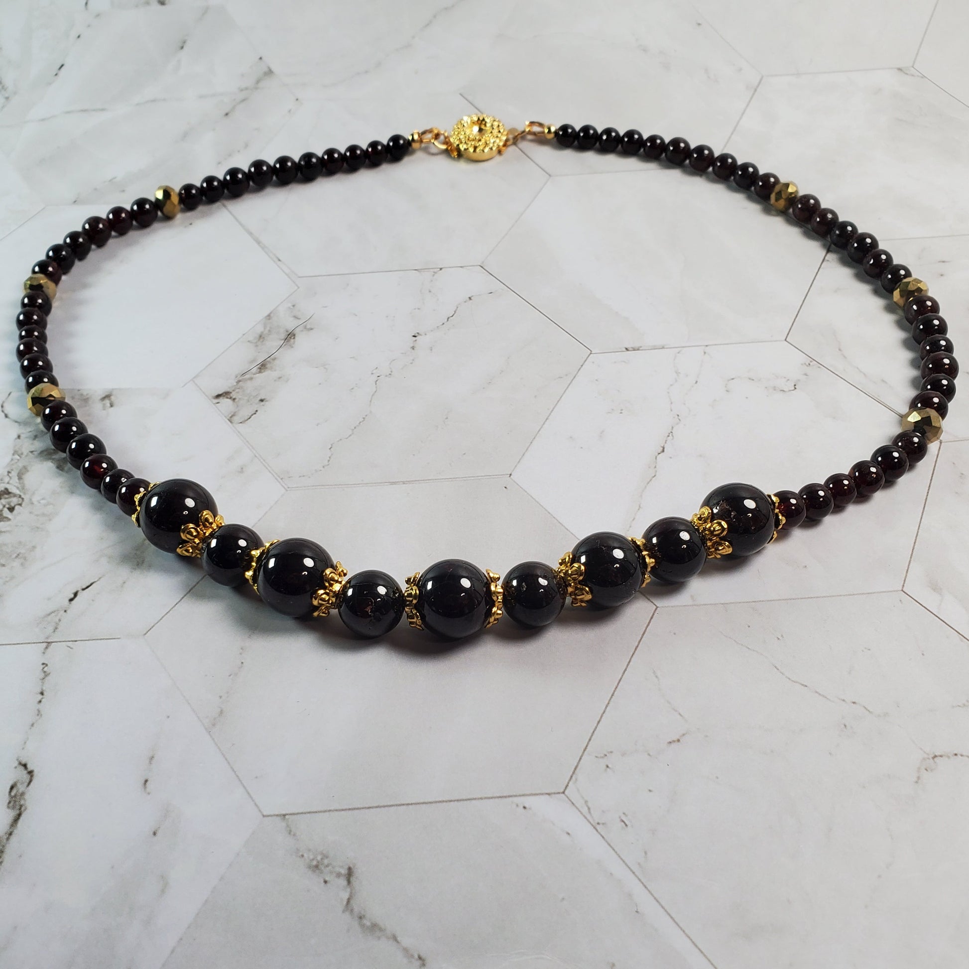 Necklace with deep red beads and gold accents on a marble surface