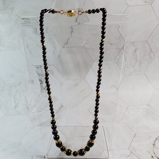 Necklace with Garnet beads and gold accents on a marble surface