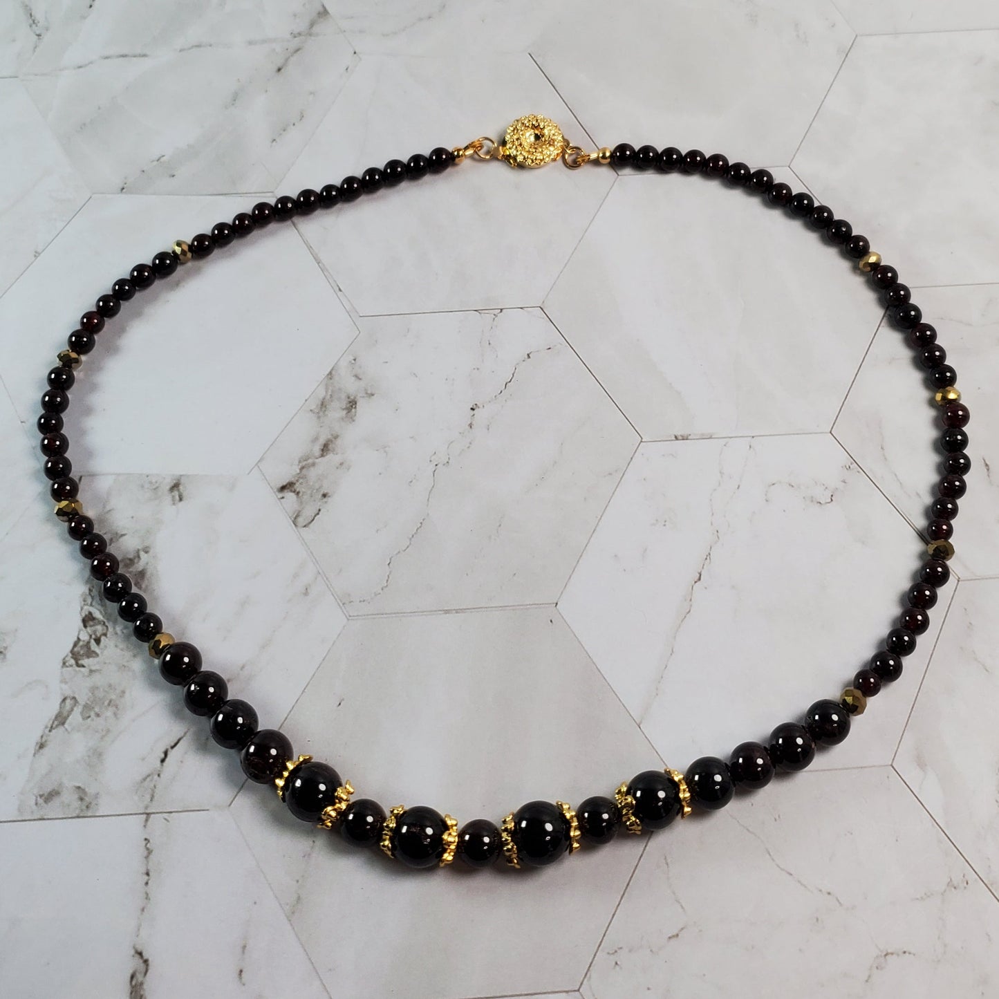 Garnet beaded necklace with gold accents on a marble surface