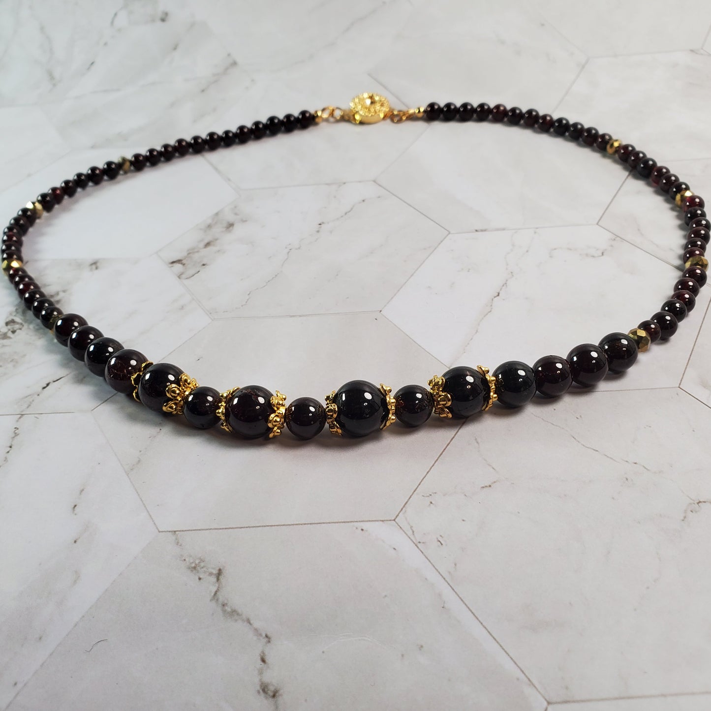 Garnet beaded necklace with gold accents on a marble surface