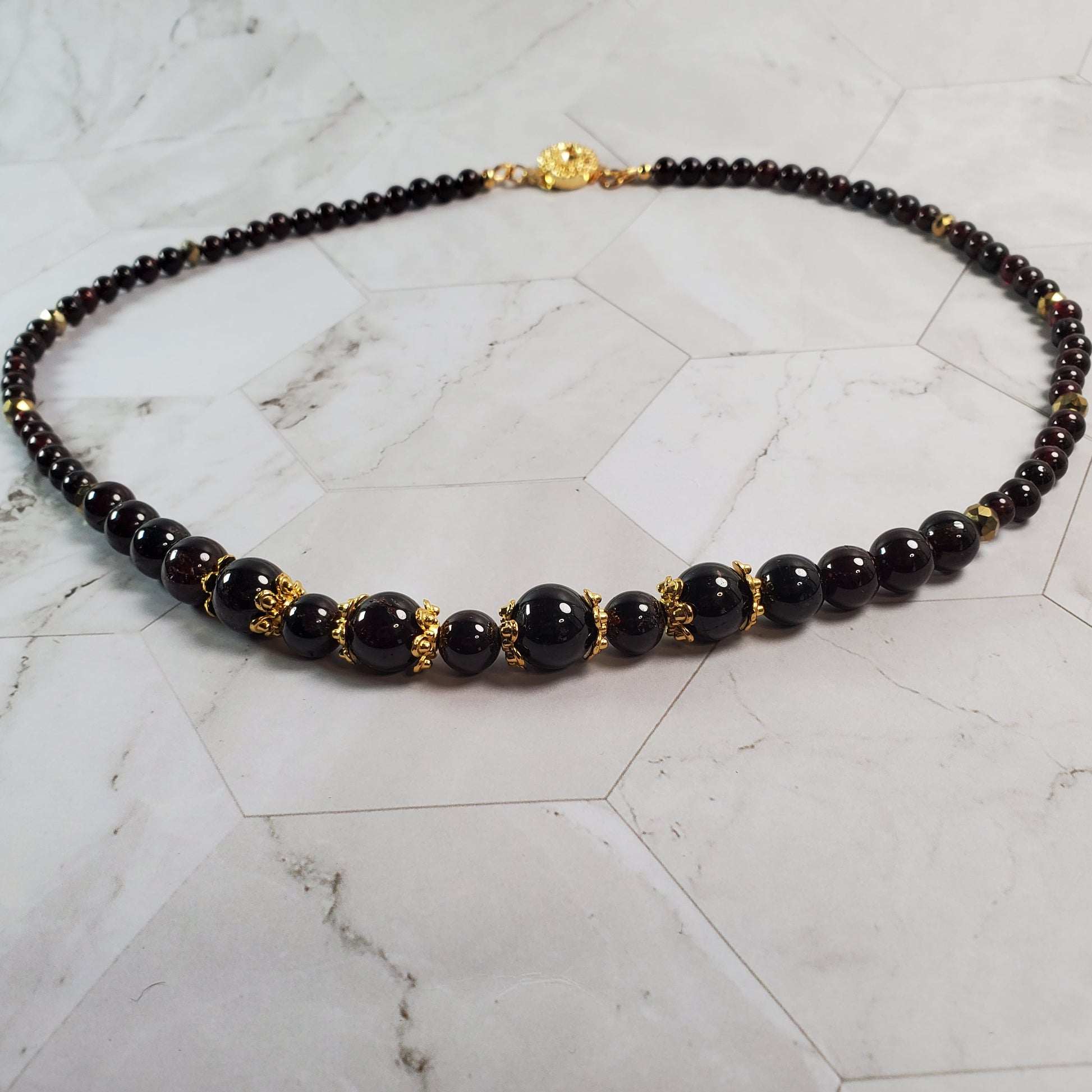Garnet beaded necklace with gold accents on a marble surface