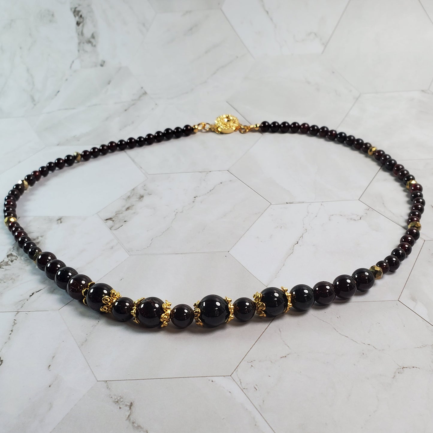 Necklace with deep red and gold beads on a marble surface
