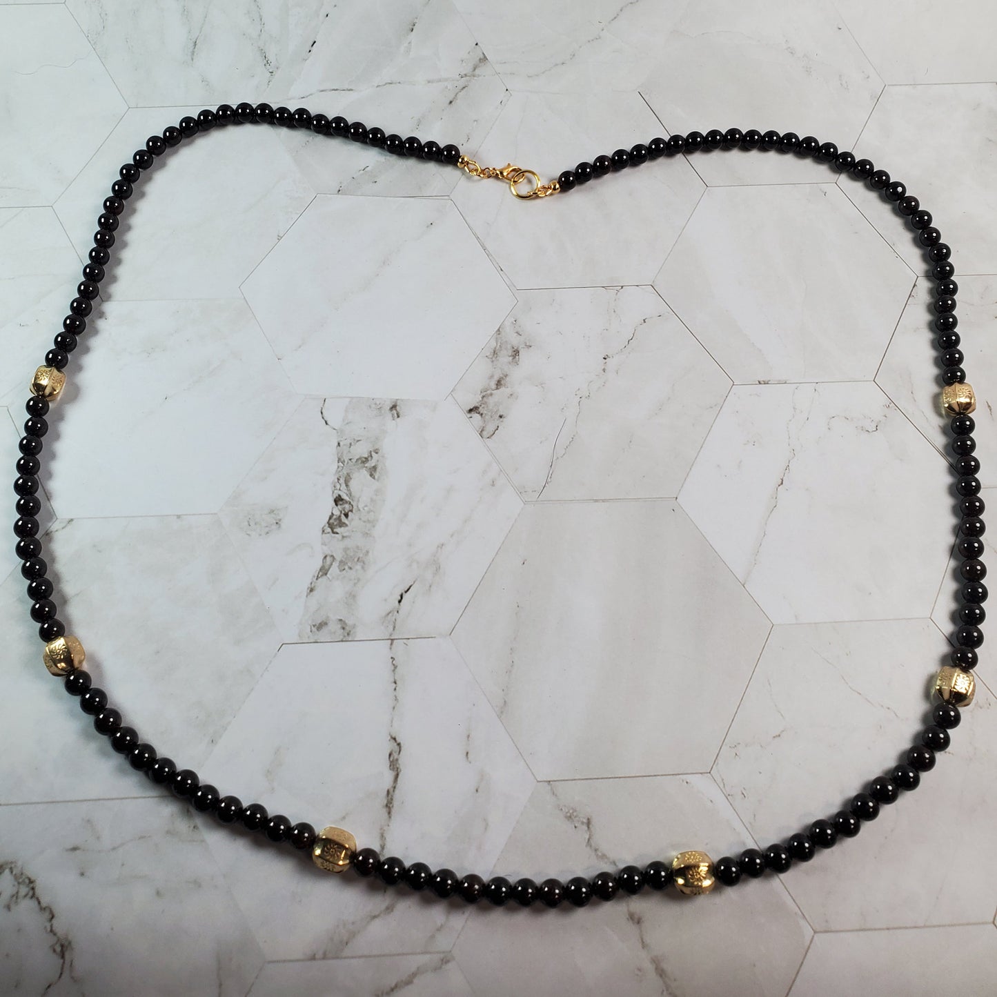 Deep red beaded necklace with gold accents on a marble surface