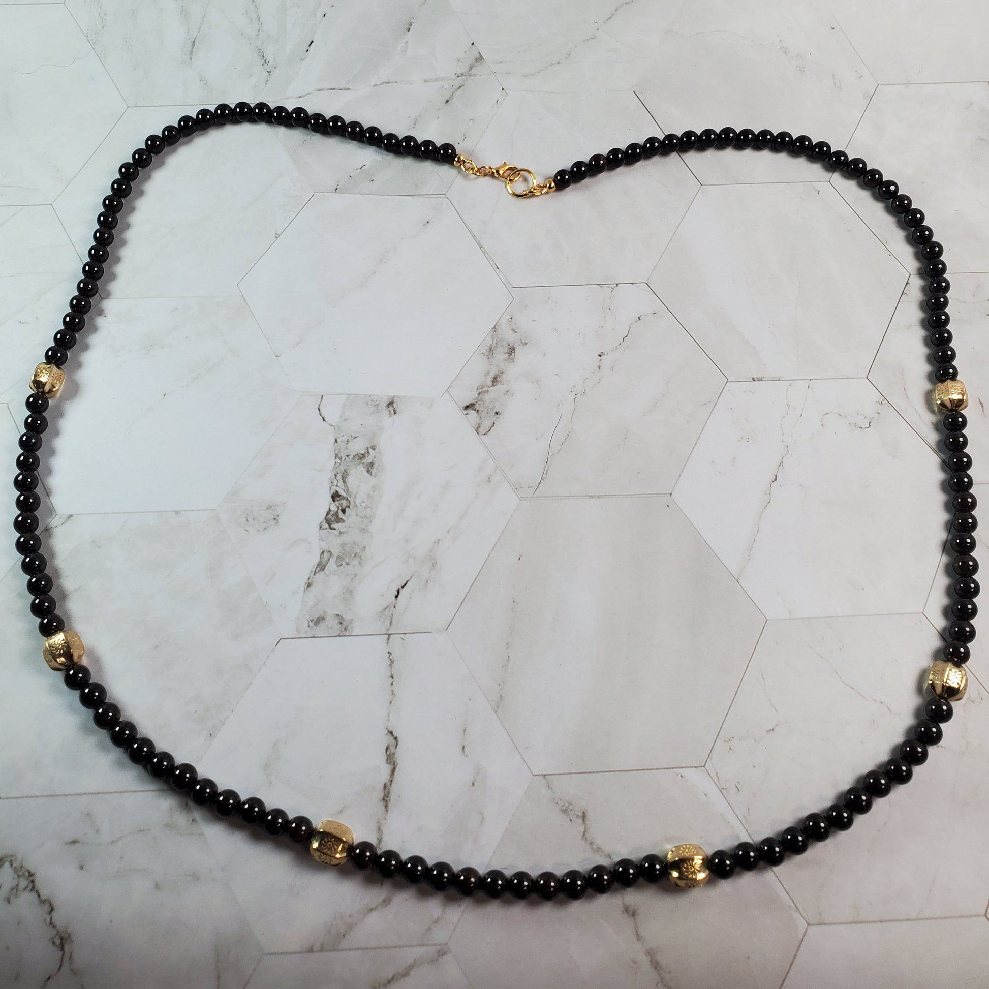 Deep red beaded necklace with gold accents on a marble surface