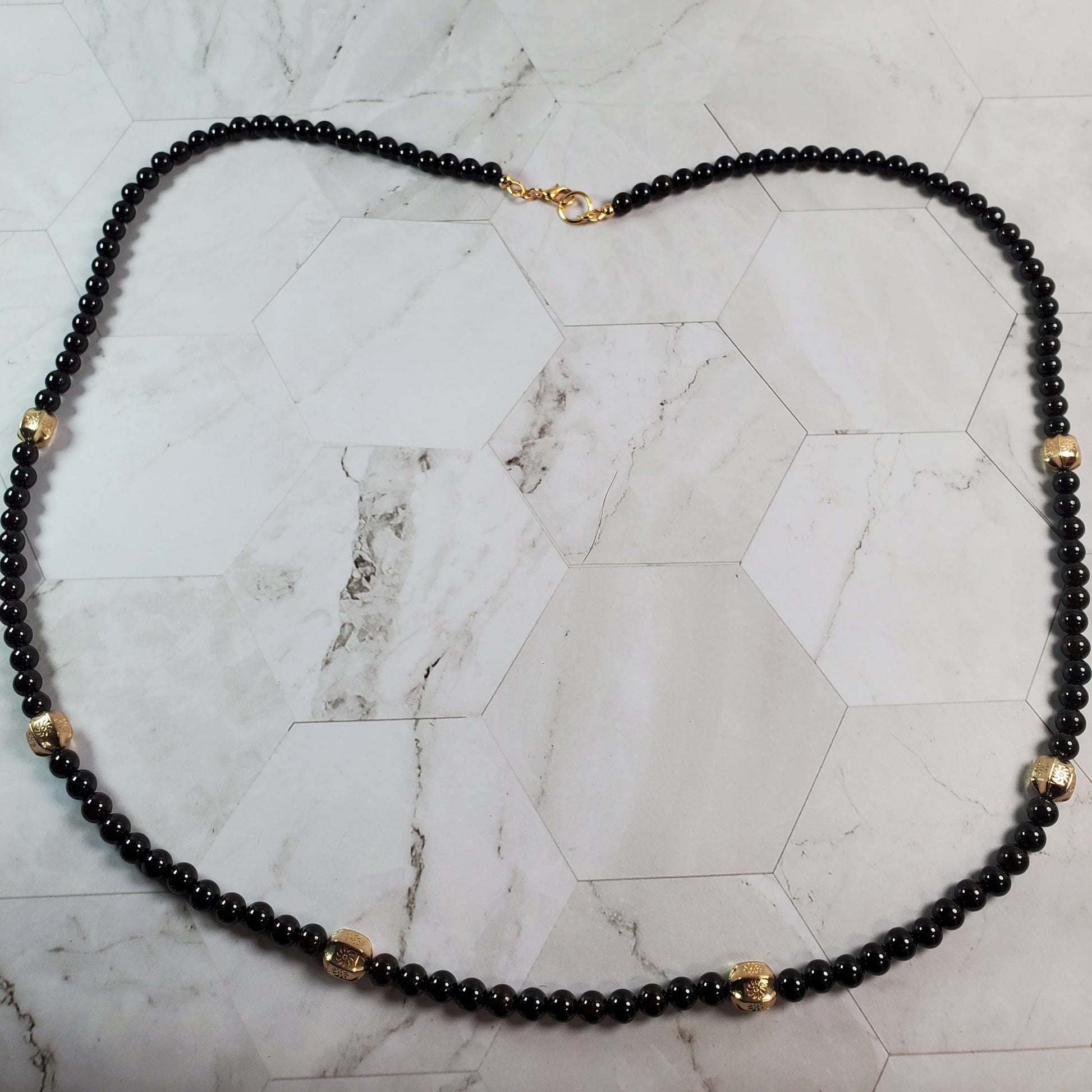 Deep red beaded necklace with gold accents on a marble surface