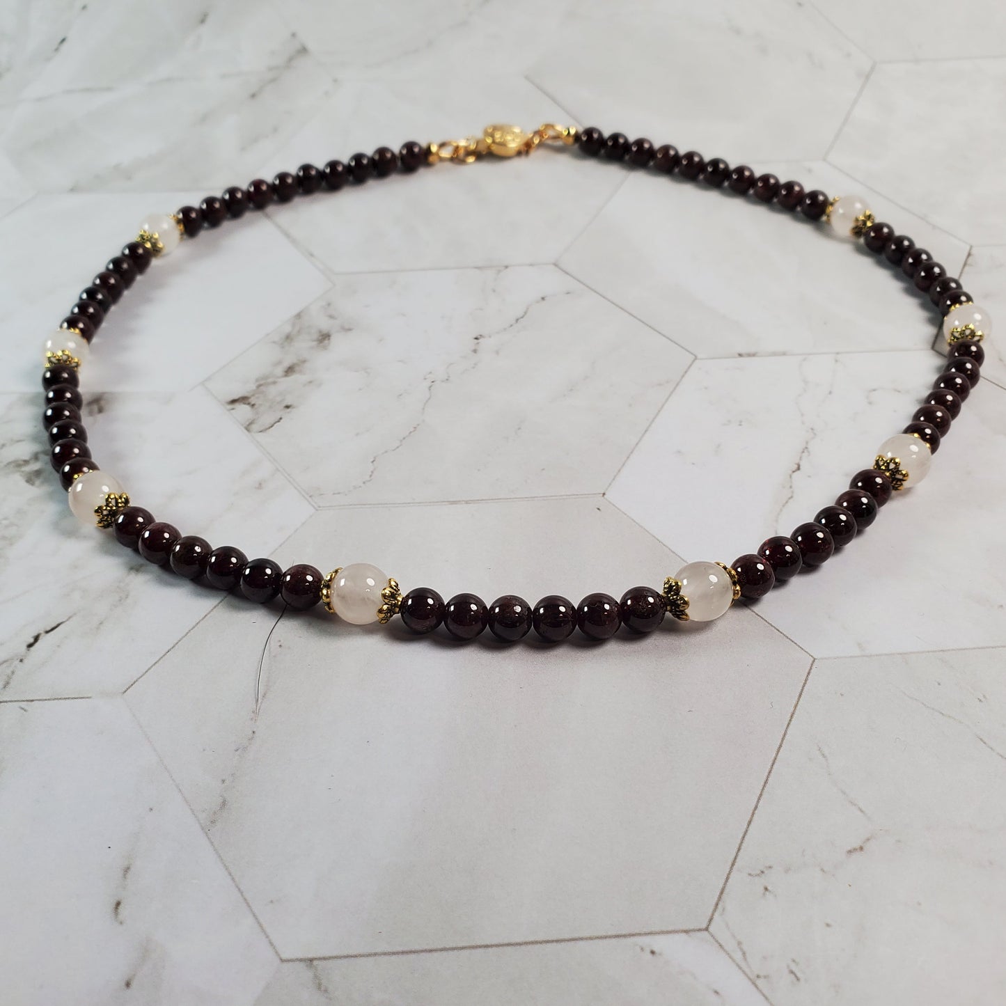 Beaded necklace with red, gold, and pink beads on a marble surface