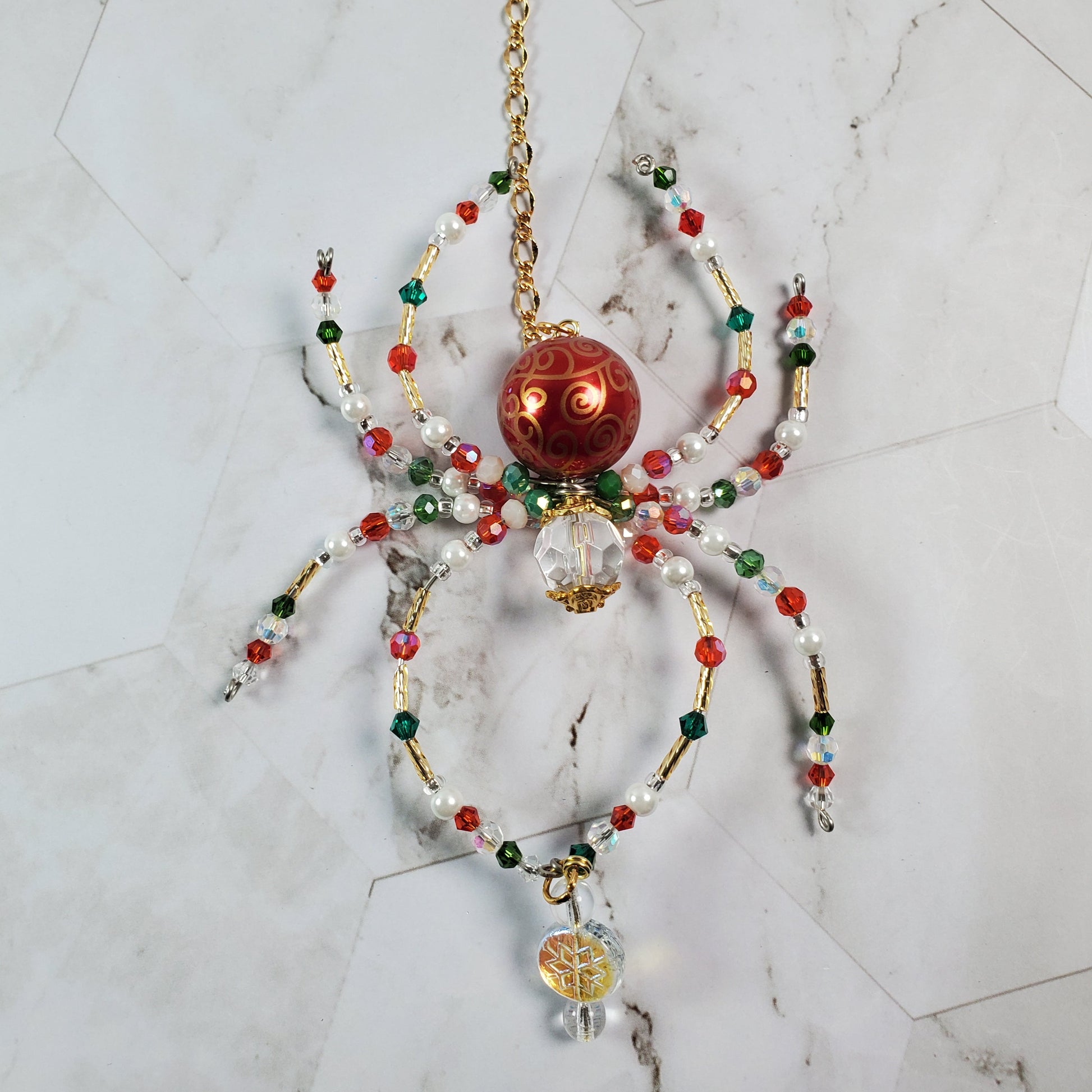 Decorative spider with red center and multicolored beads on a marble surface