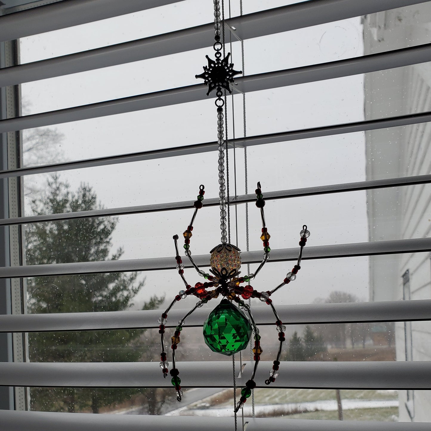Decorative spider with a green gem on a window with blinds