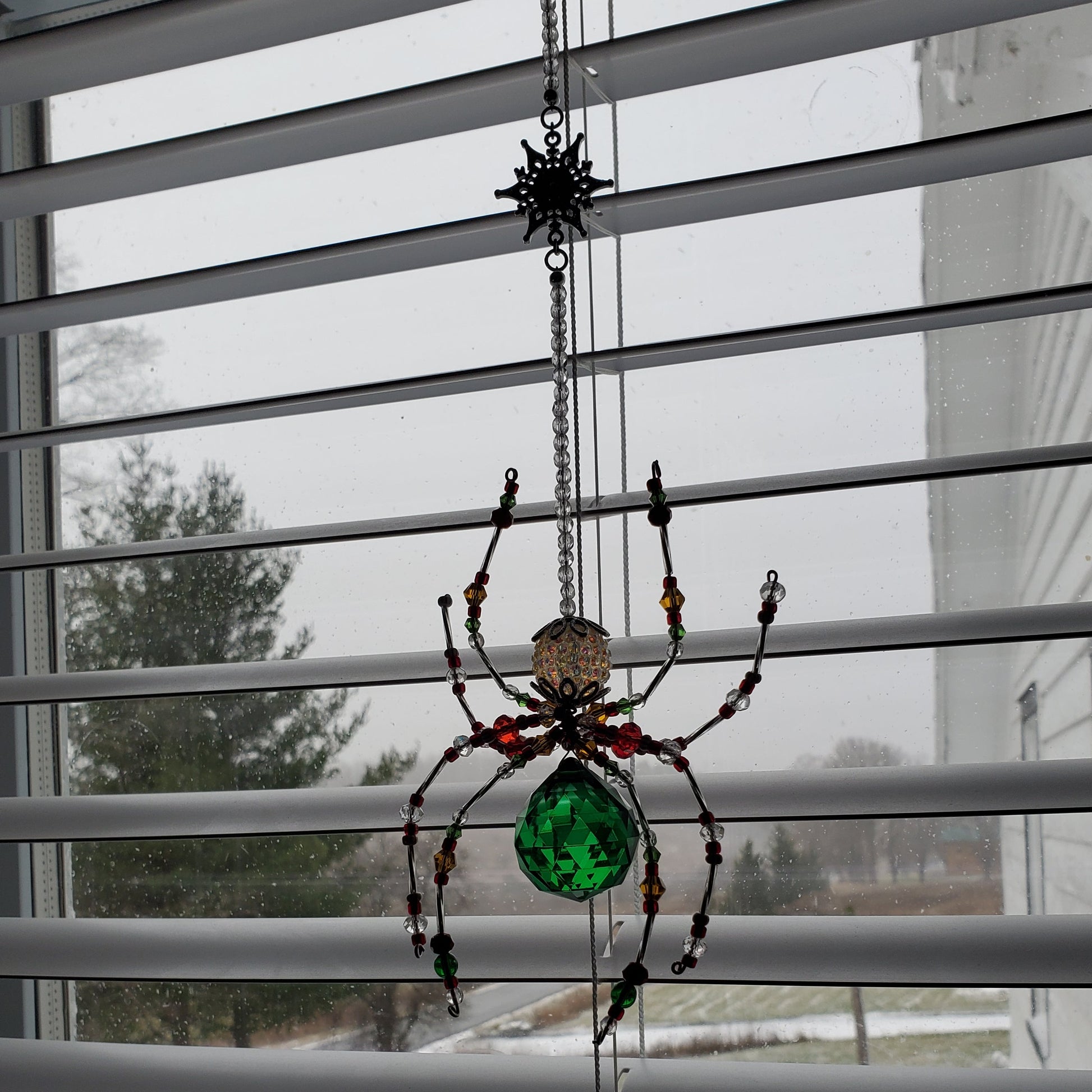 Decorative spider with a green gem on a window with blinds