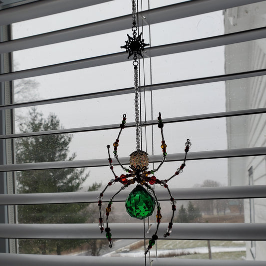 Decorative spider with a green gem on a window with blinds