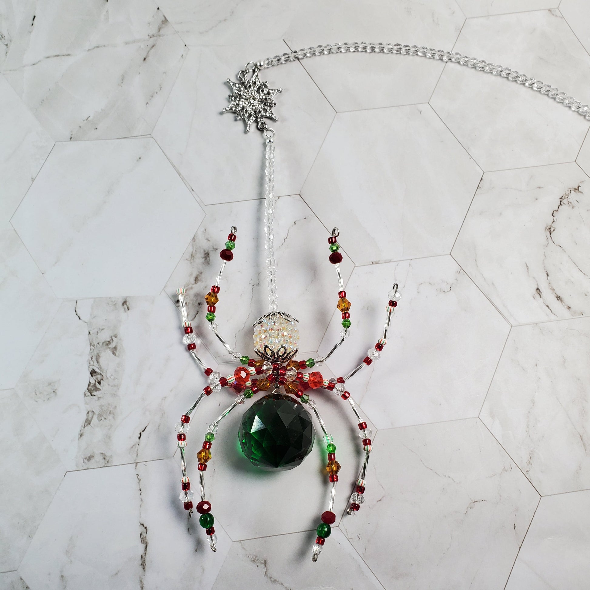 Decorative spider with beads and a green gemstone on a marble surface