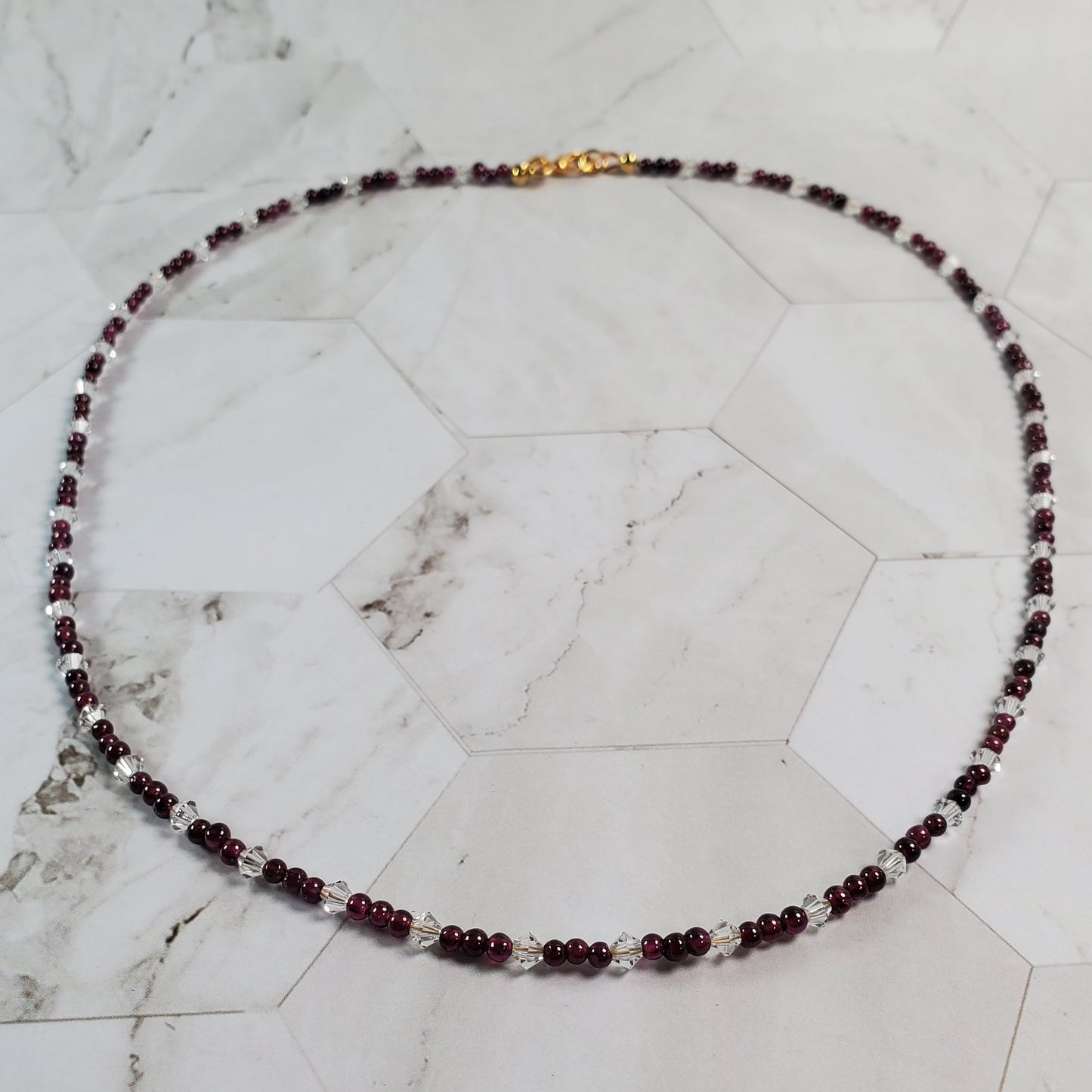 Necklace with red beads and a gold clasp on a marble surface