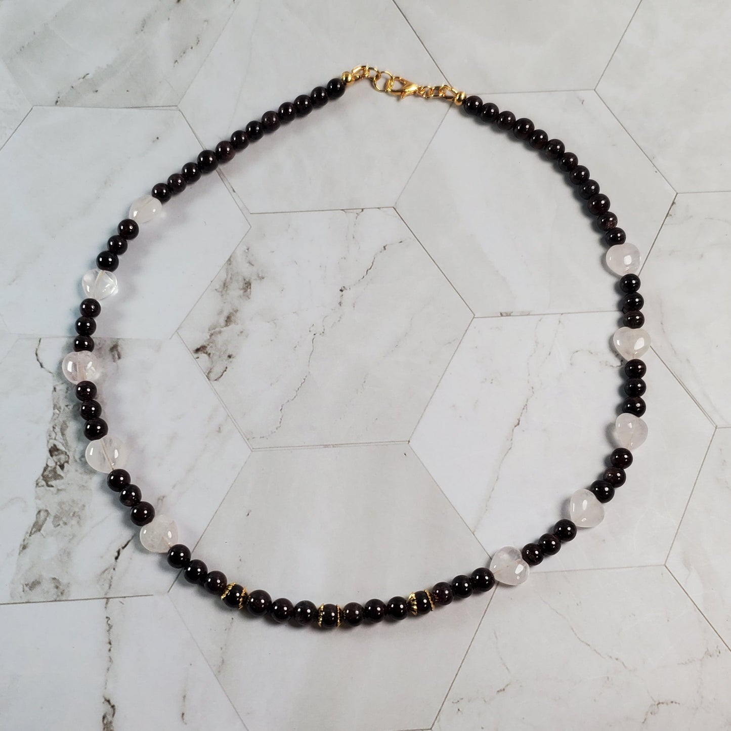 Necklace with dark red and pink beads on a marble surface.