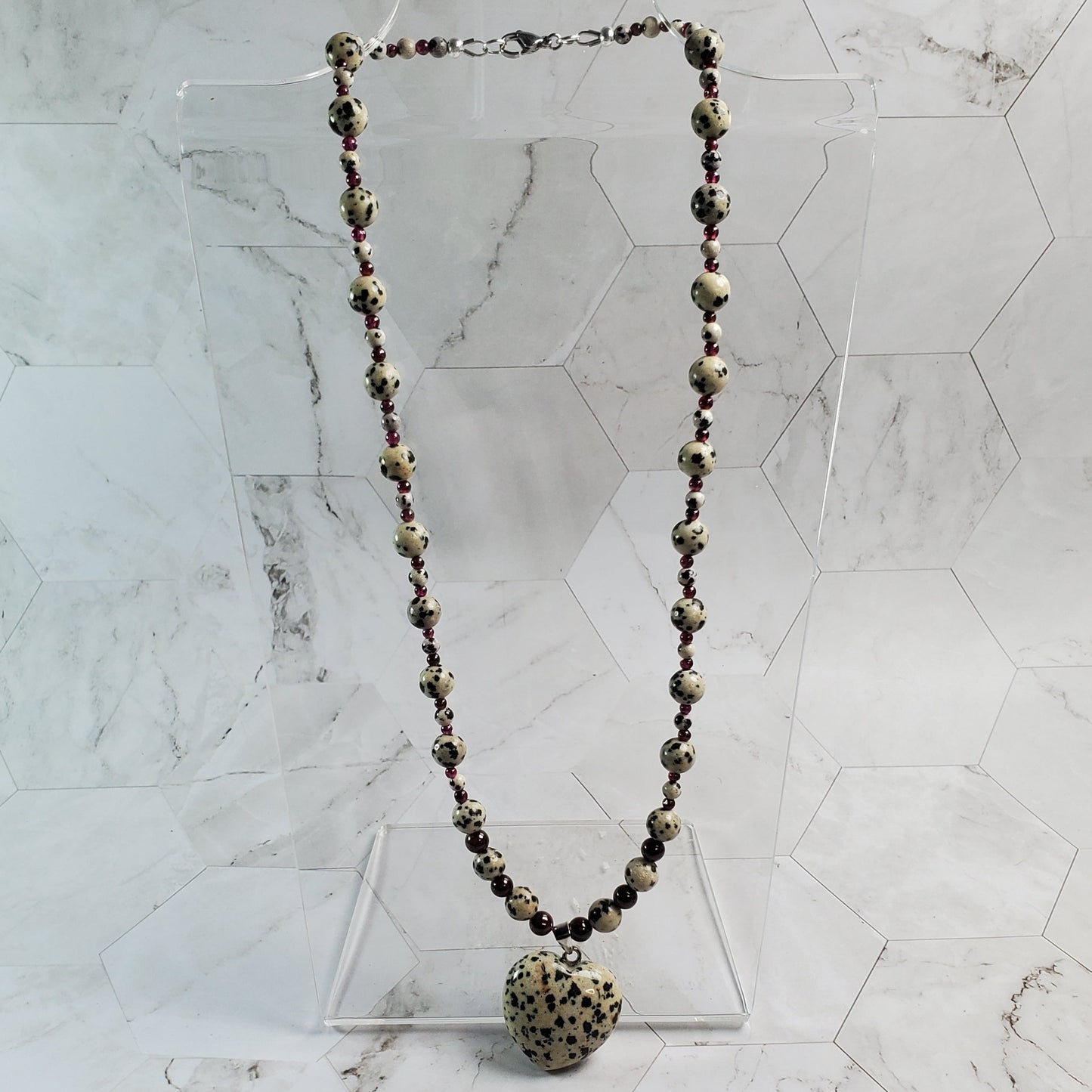 Dalmatian Jasper and Garnet Gemstone necklace on a marble tile background.