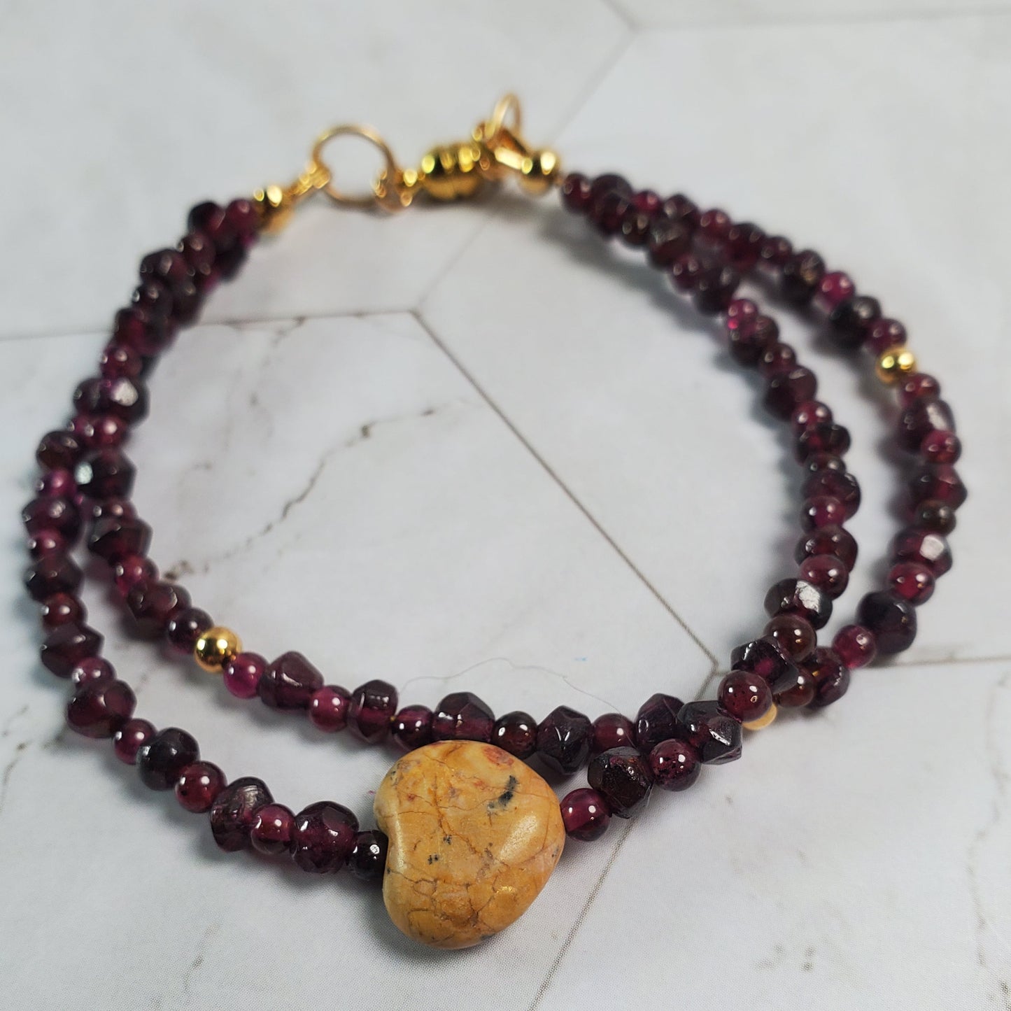 Beaded bracelet with a gold clasp and wooden charm on a light stone surface