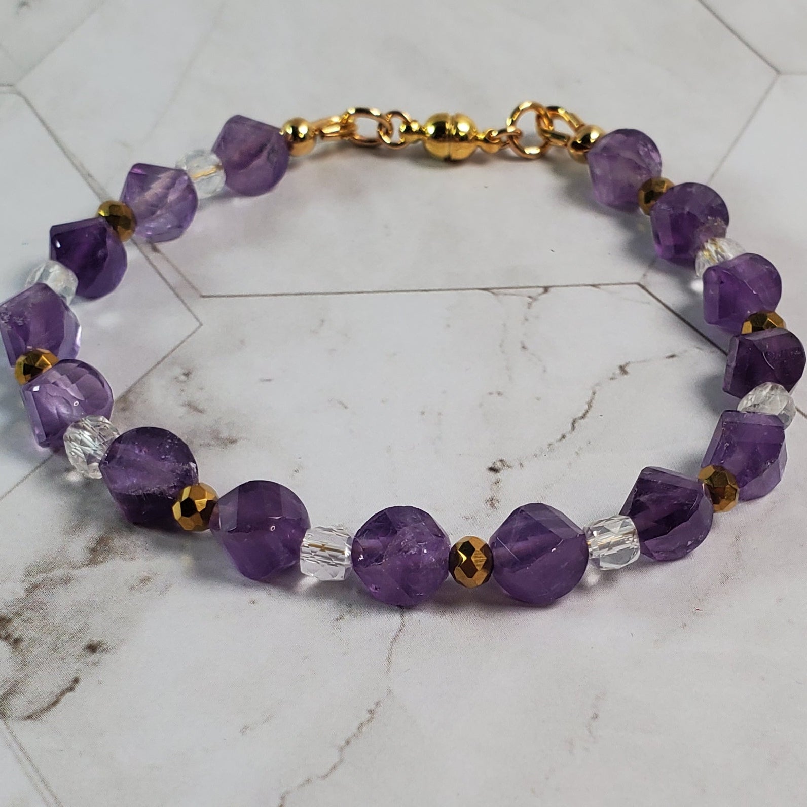 Purple beaded bracelet with gold accents on a marble surface