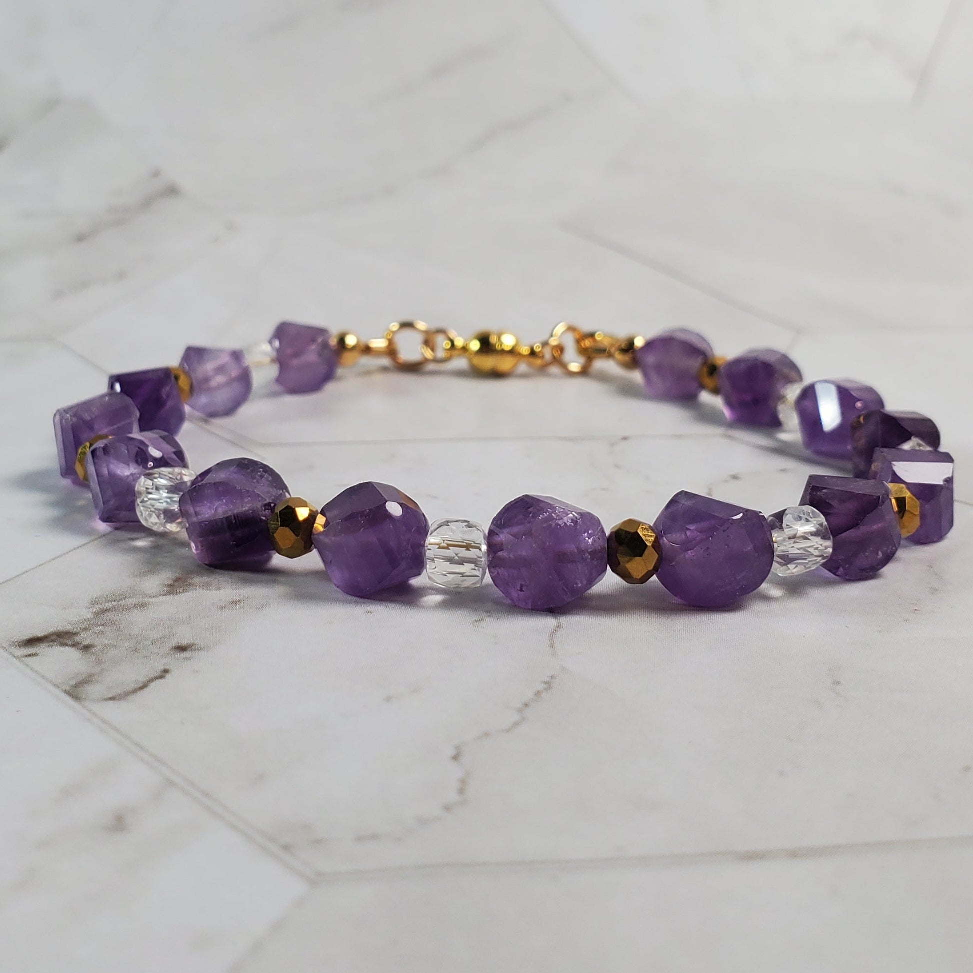 Purple beaded bracelet with gold accents on a marble surface
