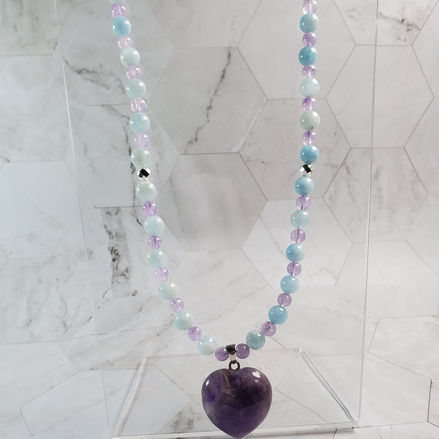 Necklace with multicolored beads and an amethyst pendant on a marble surface