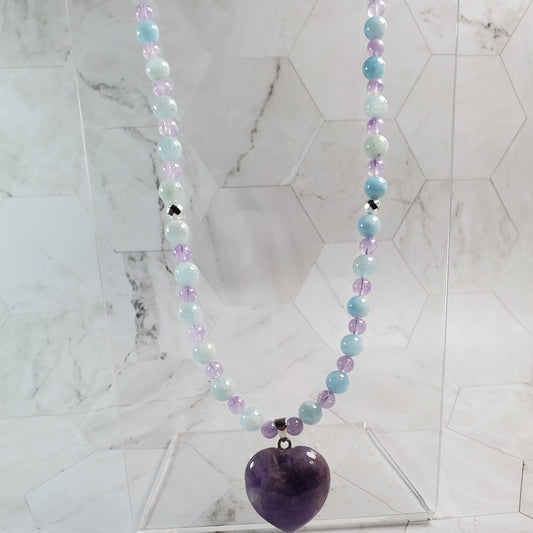 Necklace with multicolored beads and an amethyst pendant on a marble surface