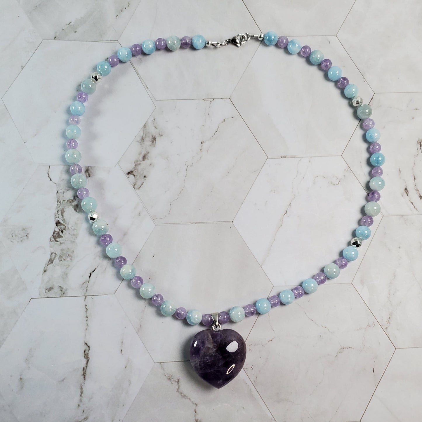 Necklace with multicolored beads and an amethyst pendant on a marble surface